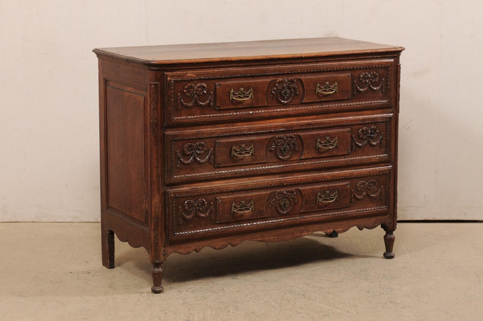 A French carved wood chest of three drawers from the early 19th century. This antique commode from France features a rectangular-shaped top with rounded front corners which rests above a case which houses three beautifully carved drawer fronts in a