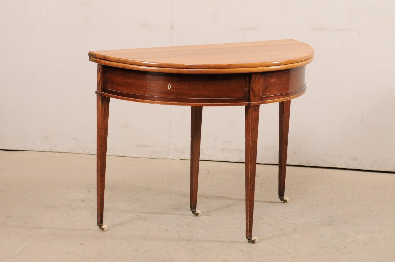 A French demi-lune wood table, which converts to a round table, from the early 19th century. This antique table from France features a half moon top over a rounded apron. The skirt is clean in design, with raised carved diamond accents above each of