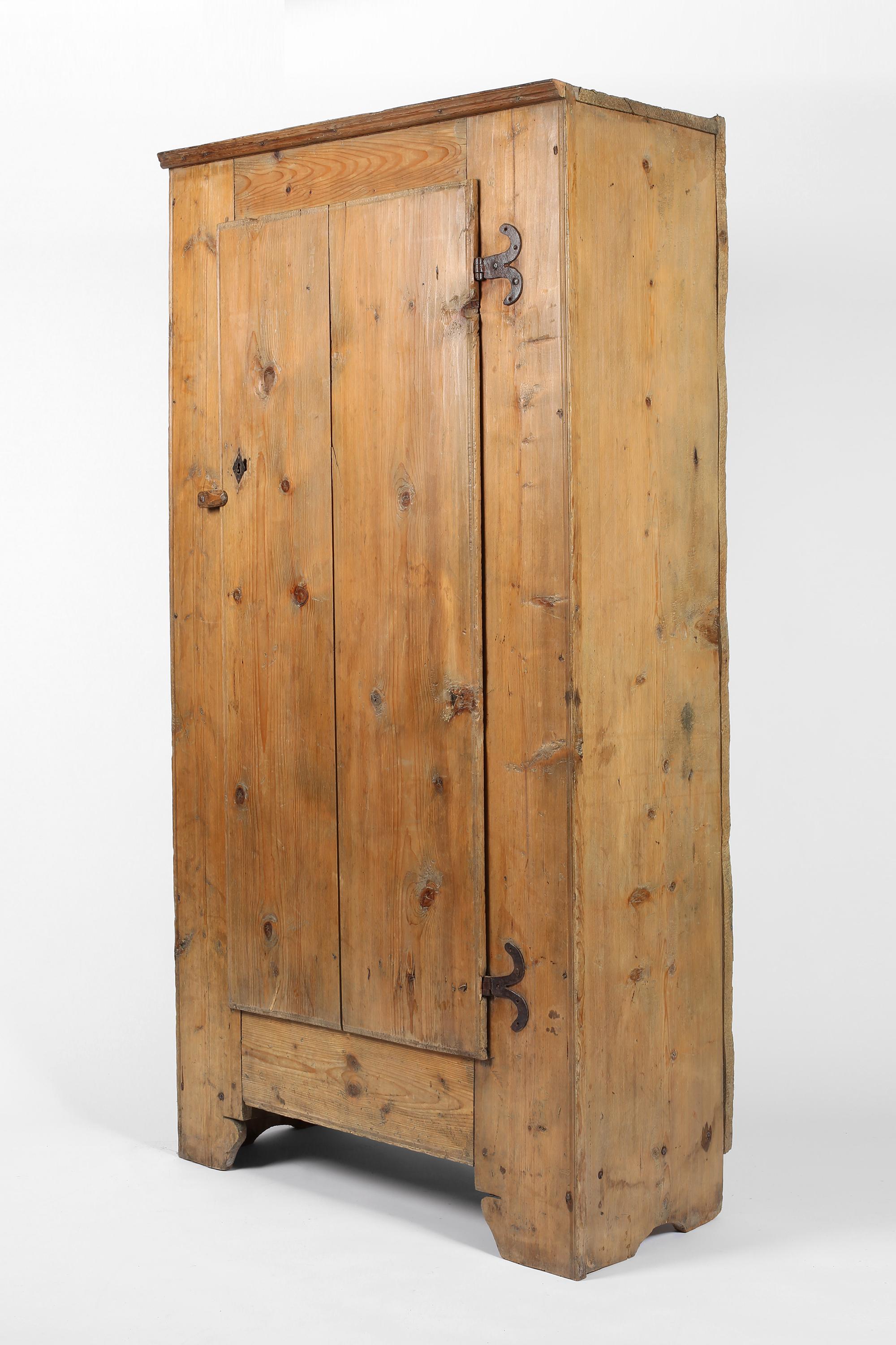A large early 19th century Alpine cupboard constructed from thick planks of pine timber. Featuring its original decorative forged iron hardware and sitting on subtly shaped feet, the two plank door opens to reveal four shelves within. French, c.