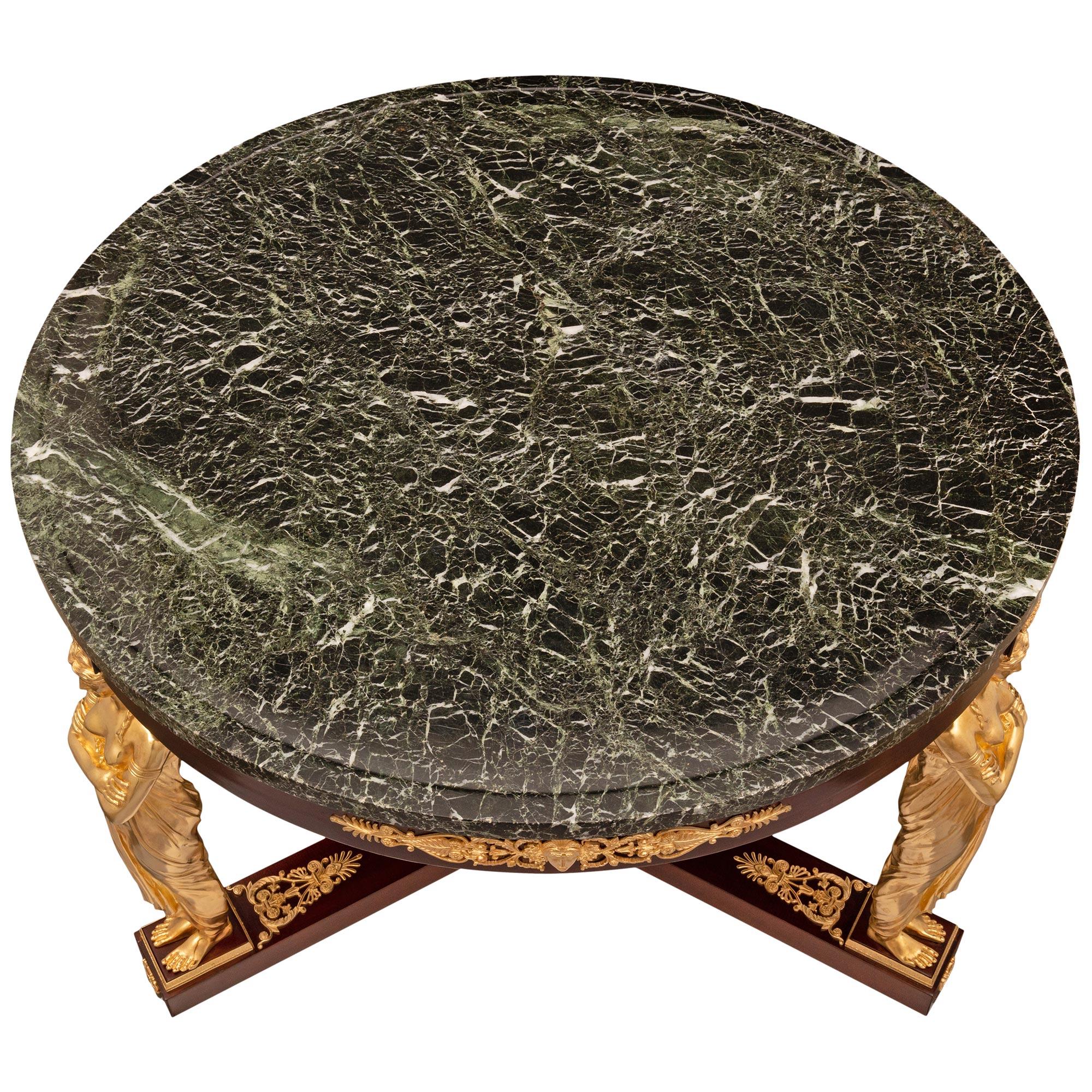 A spectacular French early 19th century Empire style mahogany, ormolu and Vert de Patricia marble center table. The most impressive circular center table is raised by three stunning ormolu supports of beautiful crossed arm maidens dressed in