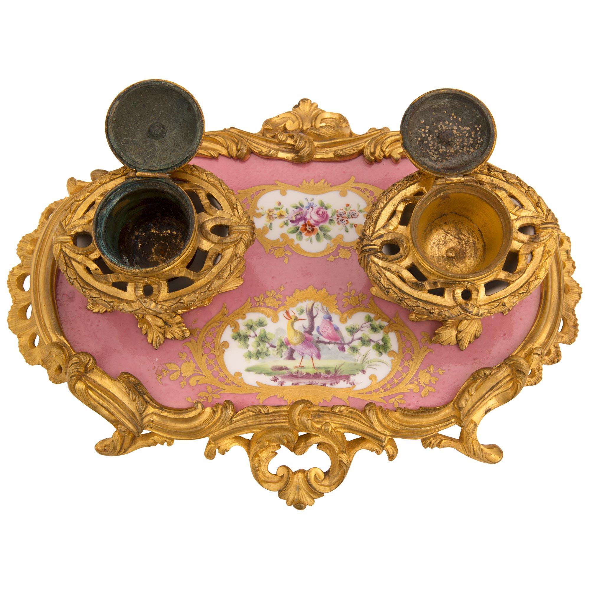 A beautiful and exceptionally high quality French early 19th century Louis XV st. Sèvres Porcelain and ormolu inkwell, signed Sèvres. The inkwell is raised by striking pierced scrolled foliate ormolu movements in a most decorative satin and