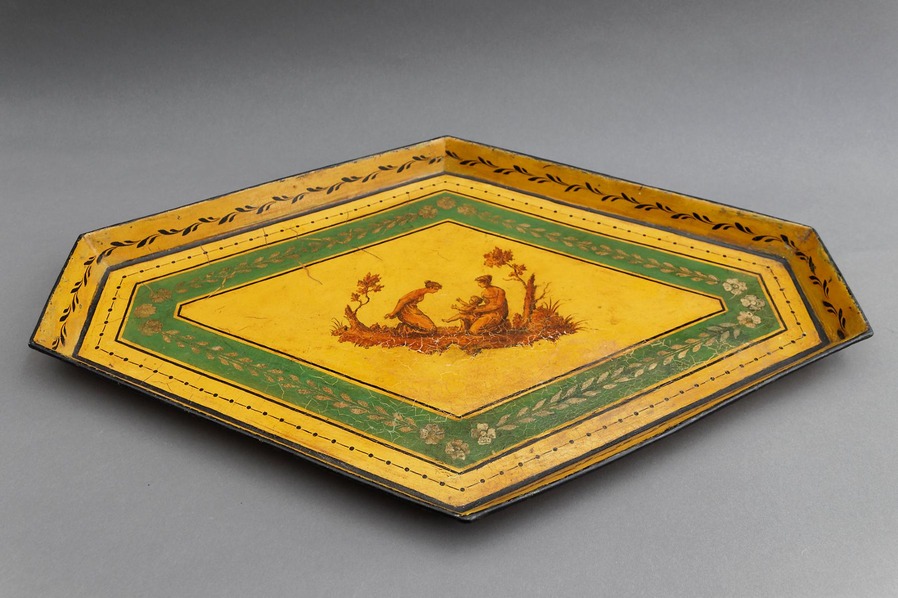 A fine and decorative polychrome painted and gilt decorated hexagonal metal tray in neoclassical style. In the centre against a yellow background two women with a child between trees. This one is fantastic and could be hung on the wall as art.