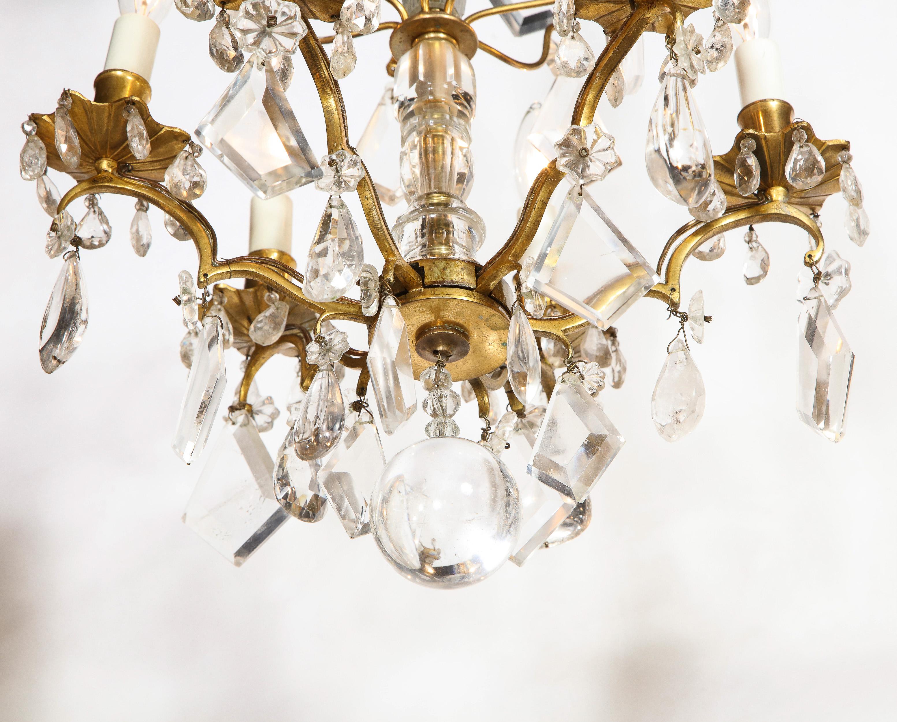 This elegant Louis XV six arm chandelier was realized in France during the early 19th century. It features a gilded bronze body with six sinuously curved undulating arms; a central sculptural stem wrapped in rock crystal; a polished tear drop finial
