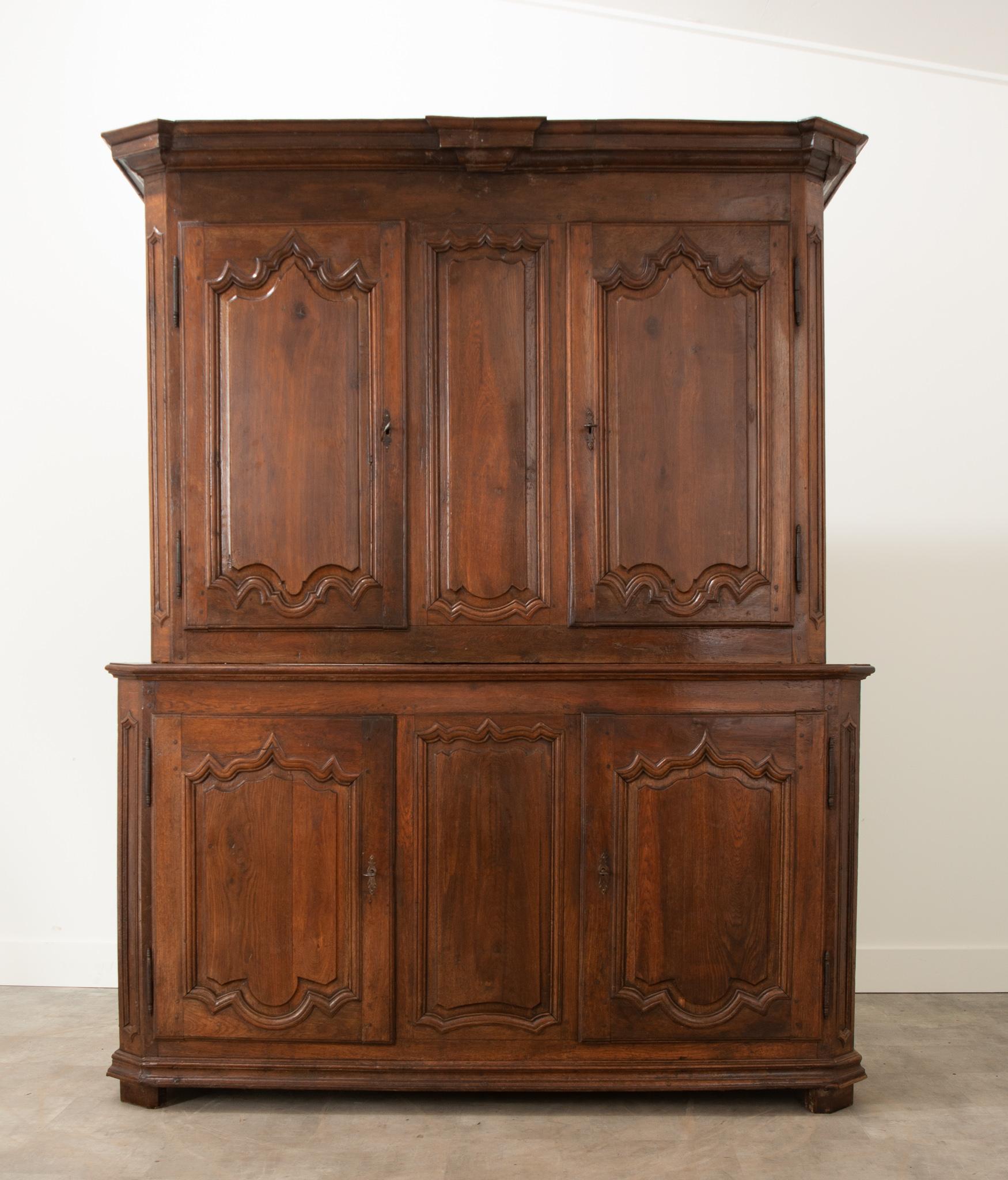 An impressive and substantial solid oak buffet a’ deux corps with Provincial charm from early 19th century France. This four door case antique is split into two bodies: a larger lower body and a smaller upper body. The upper is crowned with an