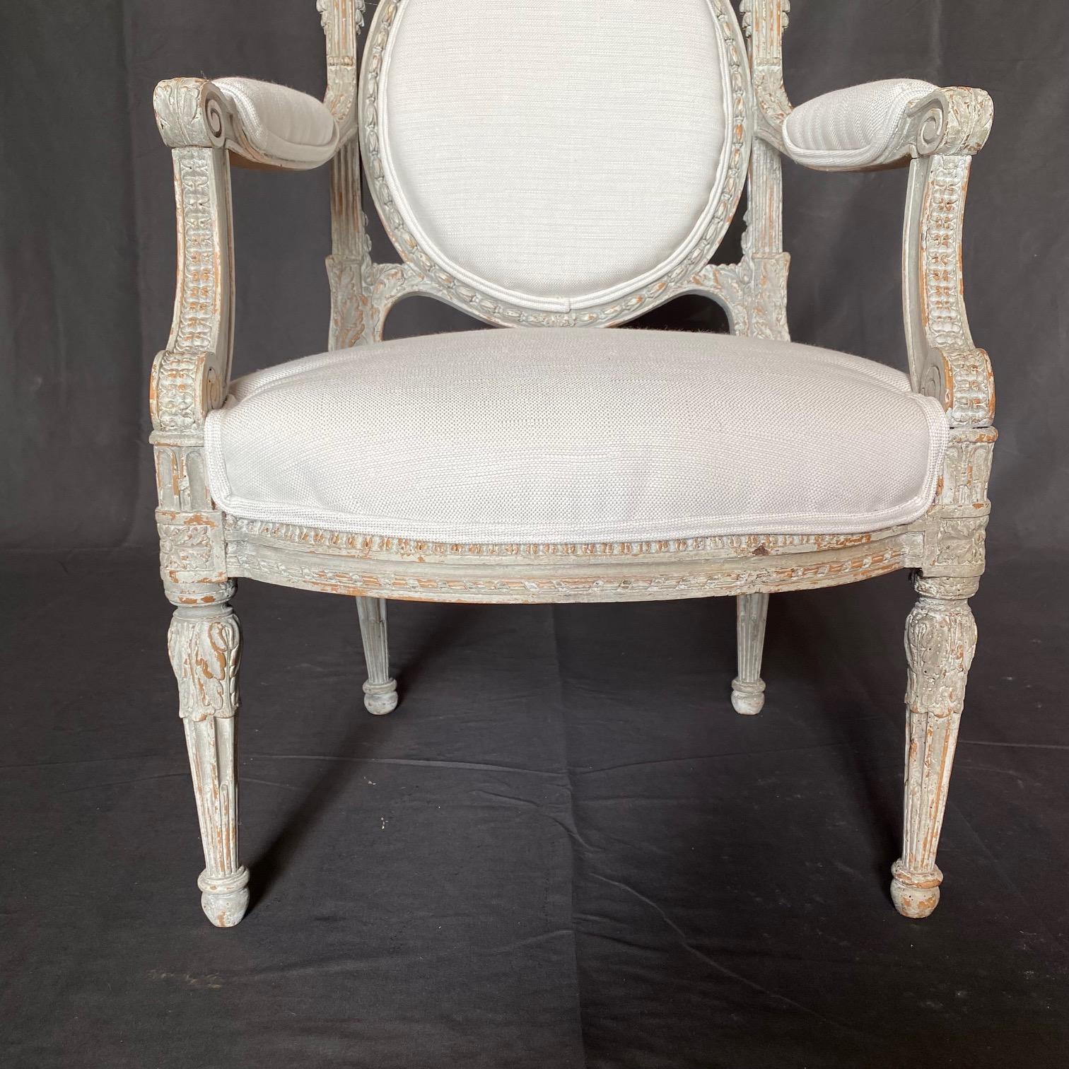 Sublimely pretty French carved and grey white painted Louis XVI fauteuil or armchair having oval back inset into intricately carved frame, with seats and armrests newly upholstered in neutral high end fabric.   Beautiful reeded tapering legs finish