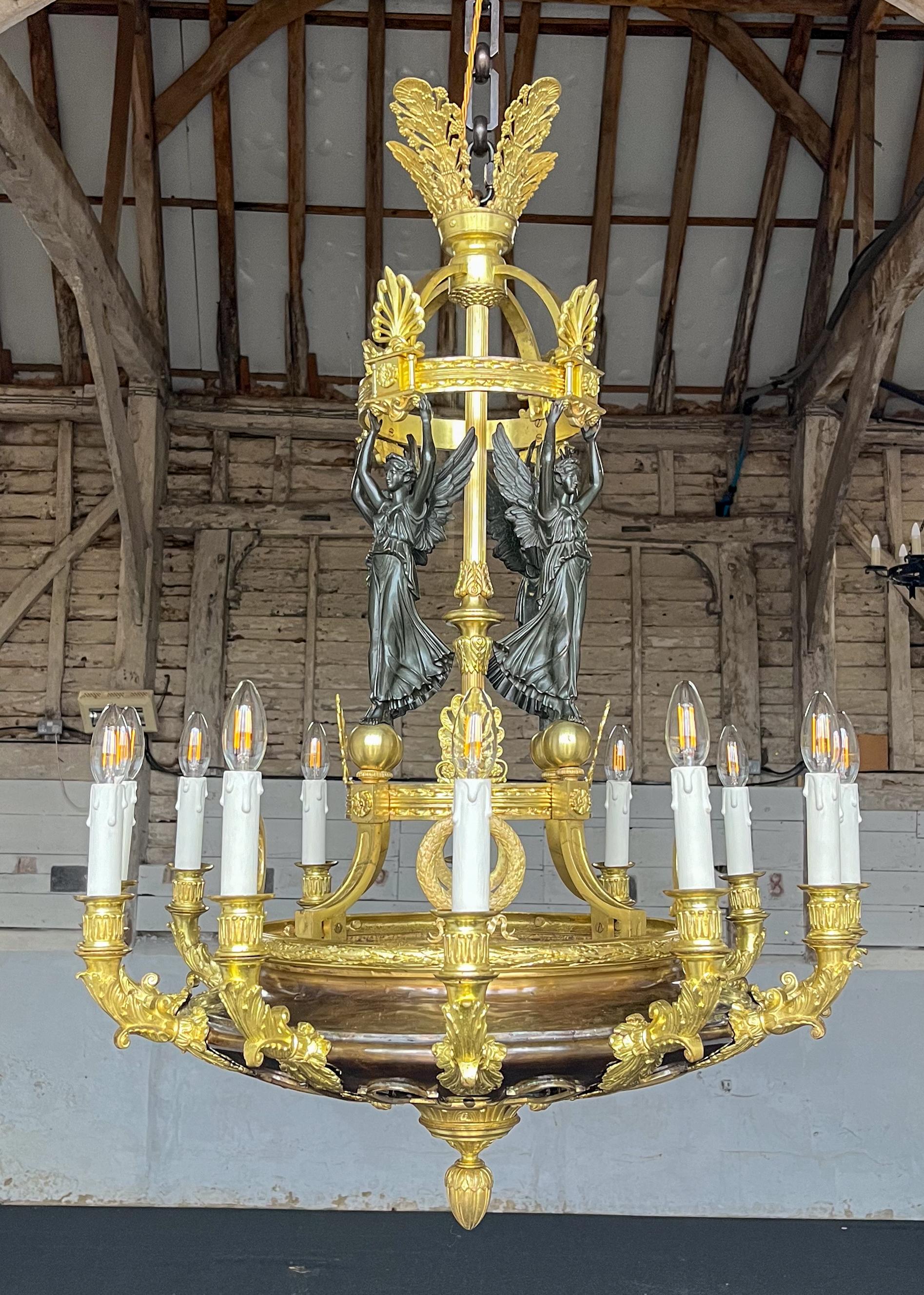 An impressive gilt and patinated bronze French Empire chandelier with twelve lights, attributed to Pierre-Philippe Thomire (1751–1843). Winged Victory figures wearing classical robes stand atop guilt spheres. 

Pierre-Philippe Thomire was a French