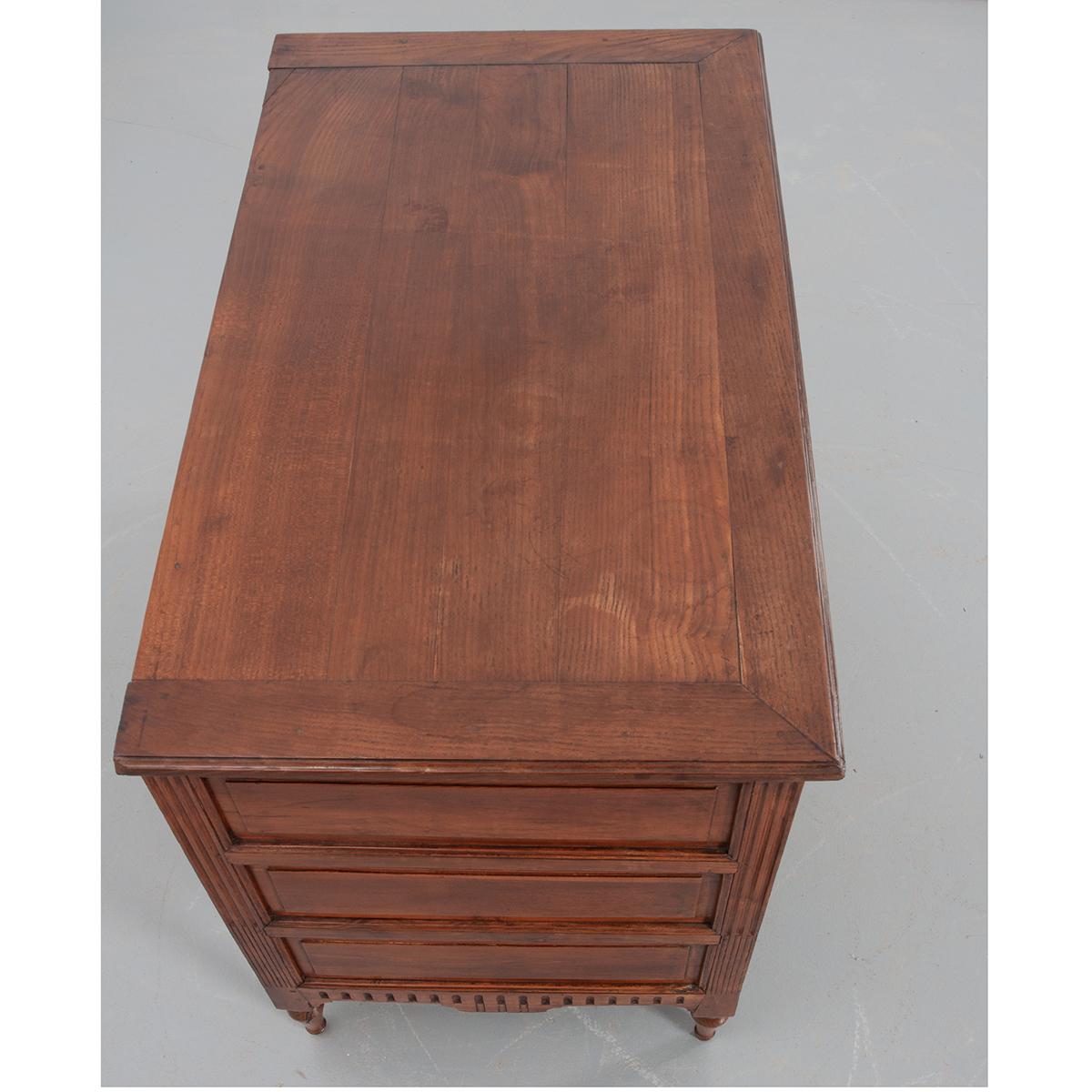 A gorgeous French walnut commode from the early 1800s. The shaped walnut top sits over the well-thought-out and detailed commode, with fluted corners, wonderful raised-panel drawer fronts and brass drawer pulls and escutcheon plates. The sides are