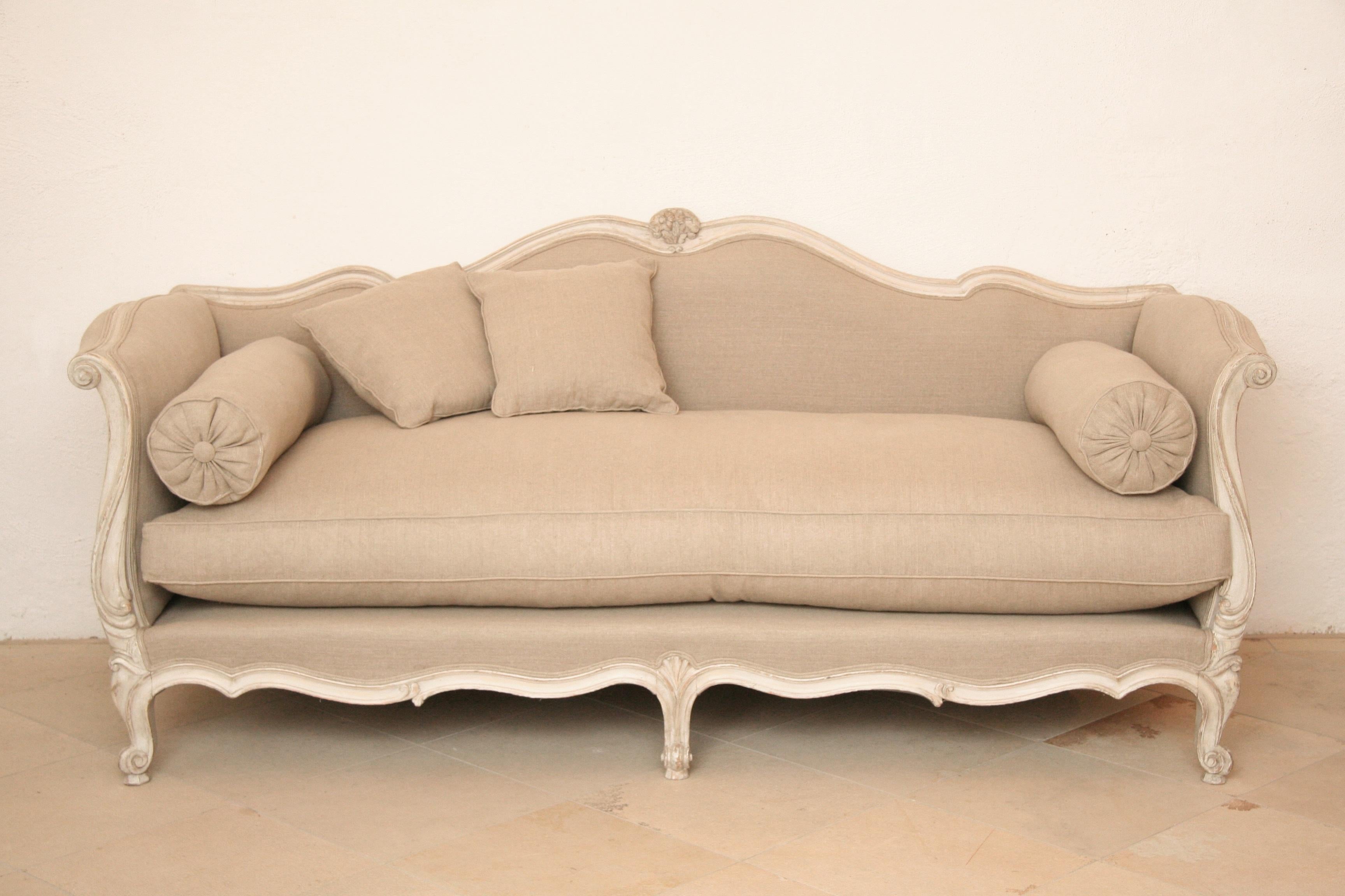 Louis Quinze sofa with a puristic note - curved frame elements with reduced decor in a cream-white color painting. 
The natural-colored linen fabric by Pierre Frey underlines the simple sophistication. 
2 side rollers belong to the object.
High