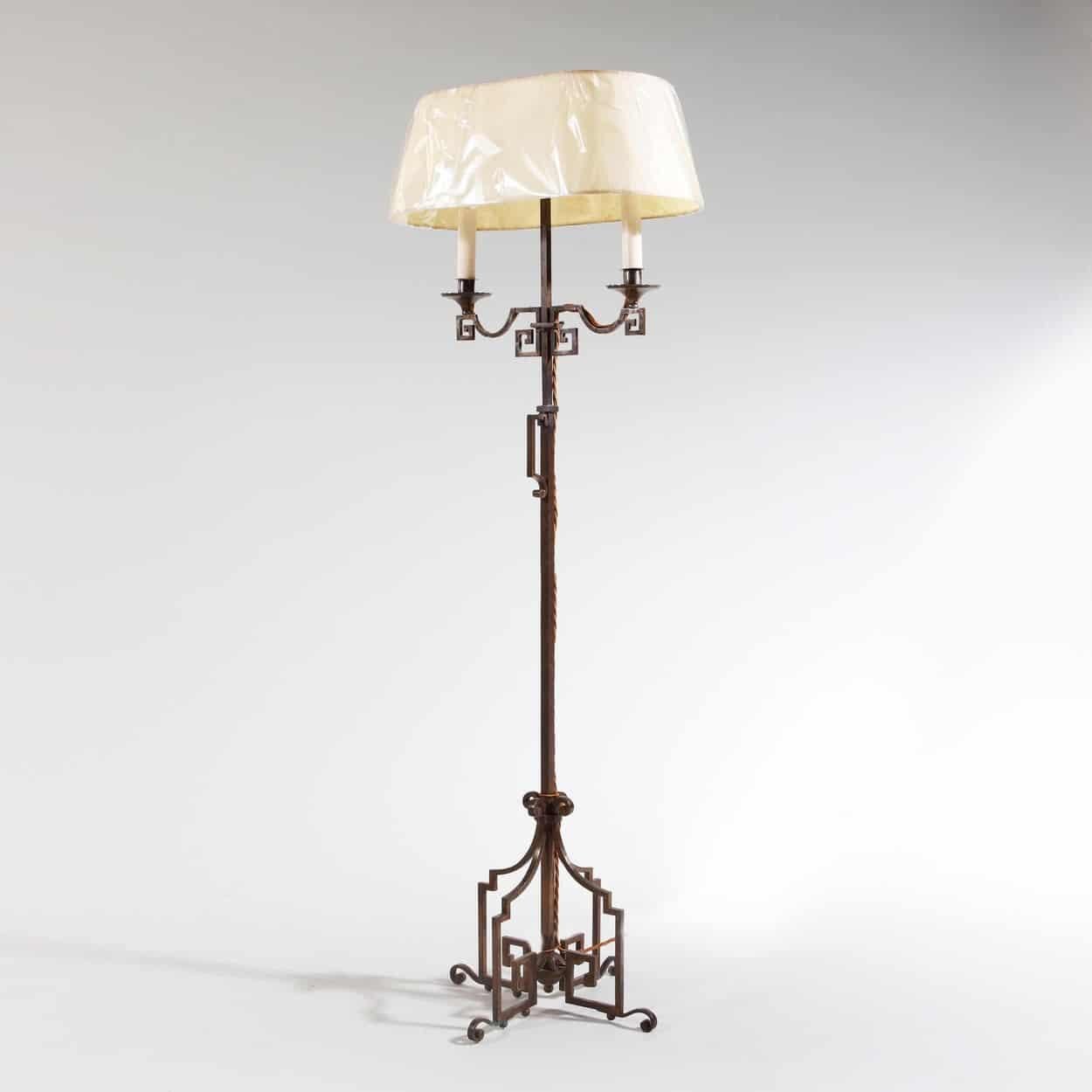 A patinated steel floor standing bouillotte lamp, the base is constructed of four facing key scrolls with foliate enrichments supporting a central stem with a carrying handle and with an adjustable height two branch shaded light above also employing