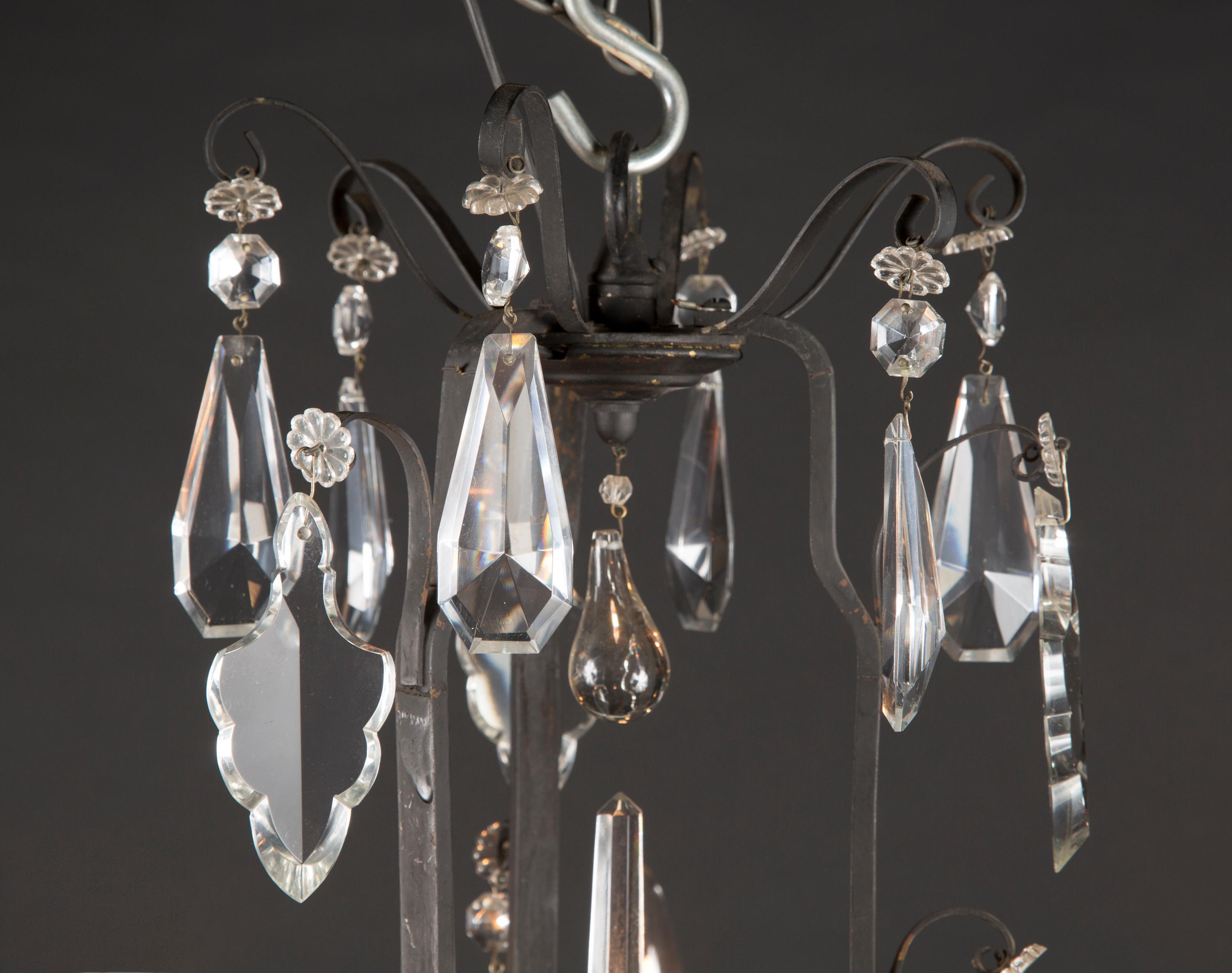 This classic early 20th century bronze chandelier comes from France and is draped in a variety of beautifully cut crystal plaquettes. Note the crystal fleurettes at top and center, the teardrop and geometric crystal interspersed throughout, and the
