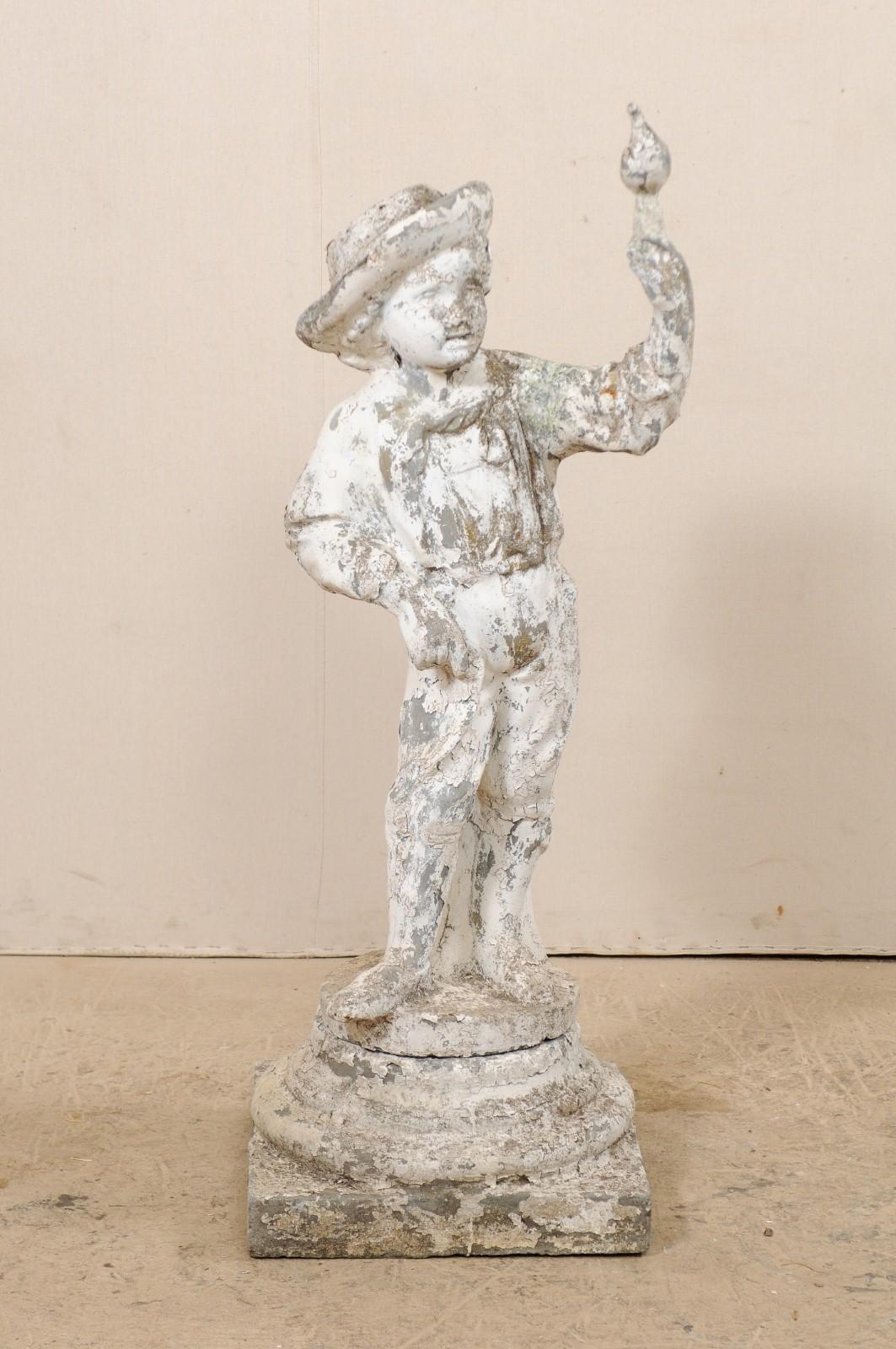 A French cast-stone garden sculpture of boy with bird from the early 20th century. This antique statue from France, of cast-stone, features a young boy, standing against a small tree trunk, with hand raised and bird perched atop. This sculptural