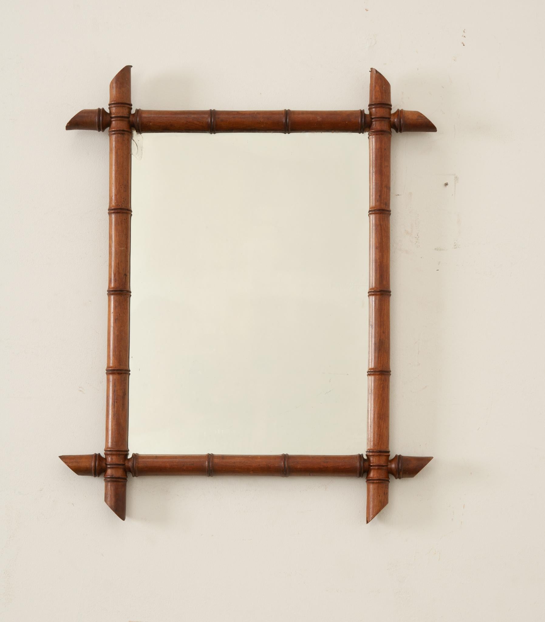 A French faux bamboo mirror circa 1900 with slanted accents, rich brown patina, and chic style. This mirror invites the opulence of history into your interior and is a nod to turn of the century elegance and charm.  The mirror’s wood frame has been