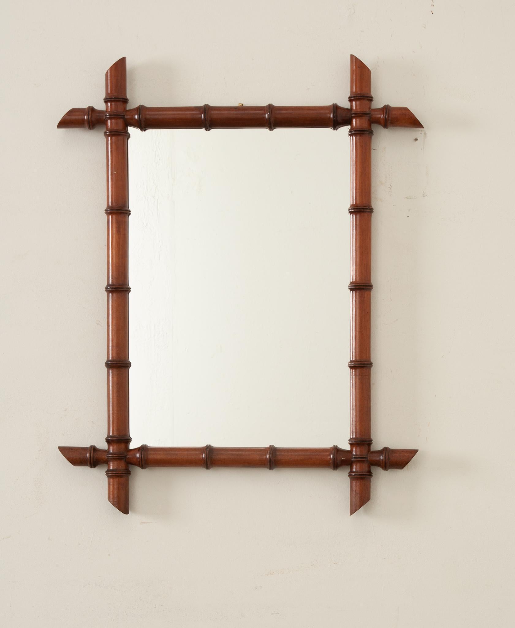 A French faux bamboo mirror circa 1900 with slanted accents, rich brown patina, and chic style. This mirror invites the opulence of history into your interior and is a nod to turn of the century elegance and charm. The mirror’s wood frame has been