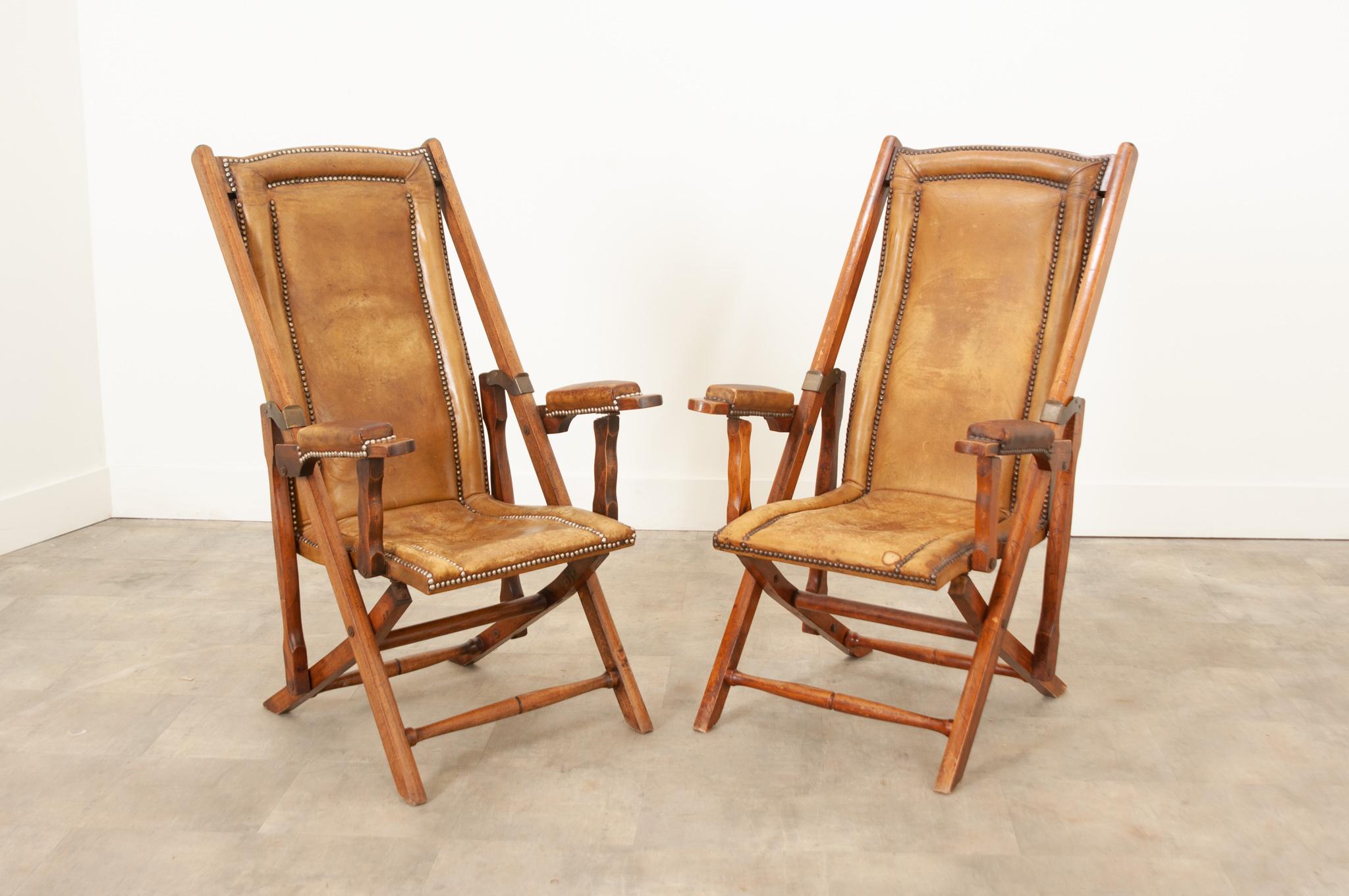An exceptional and rare pair of French campaign chairs hand-crafted in France circa 1900. A stunning set of military campaign folding chairs with original worn leather and nailhead trim with padded back rest, seats, and arm rests within expertly