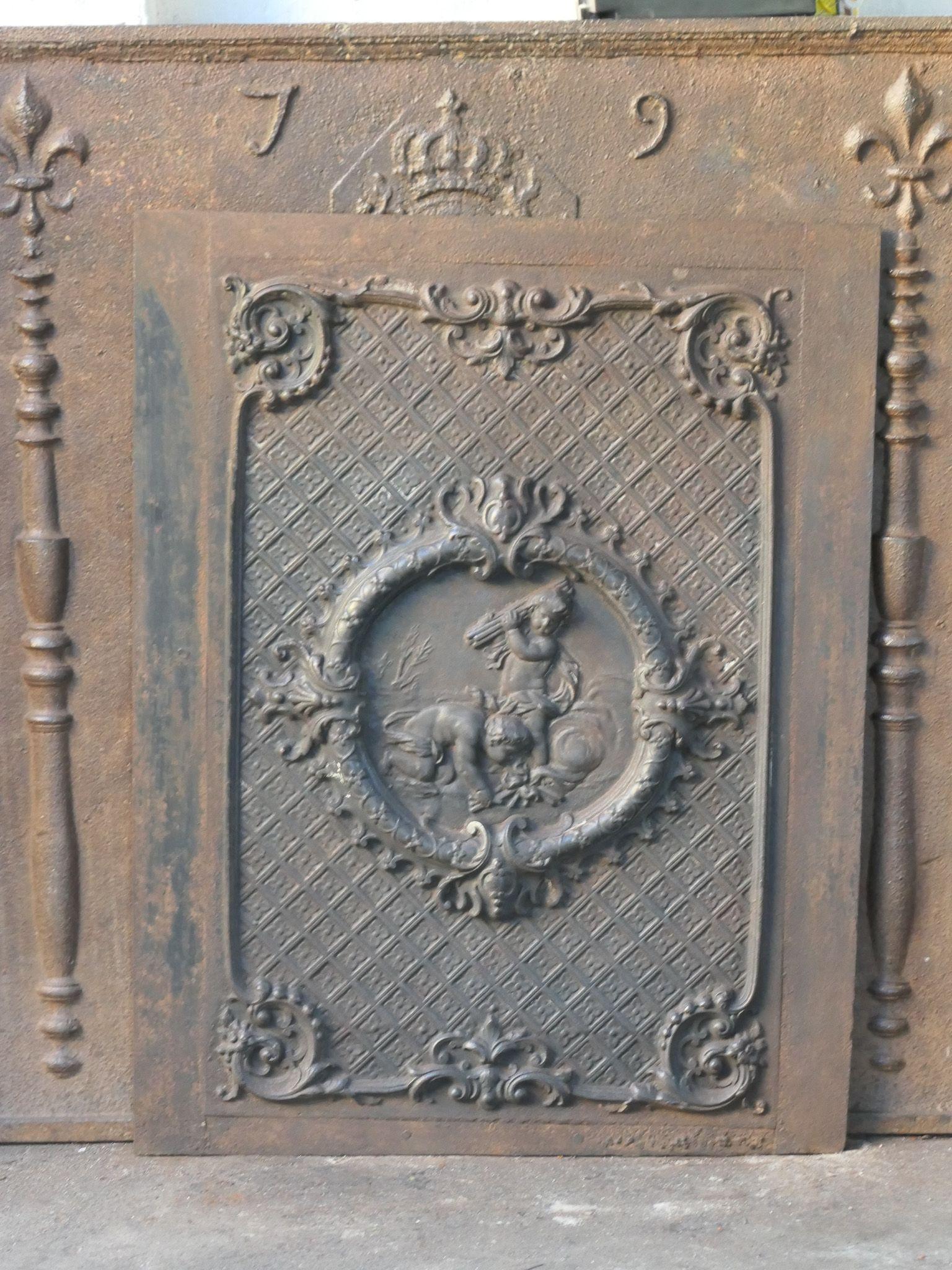 Early 20th Century French Napoleon III style fireback with two cupids. The fireback is made of cast iron and has a natural brown patina. Upon request, it can be made black / pewter. It is in good condition, without cracks.
