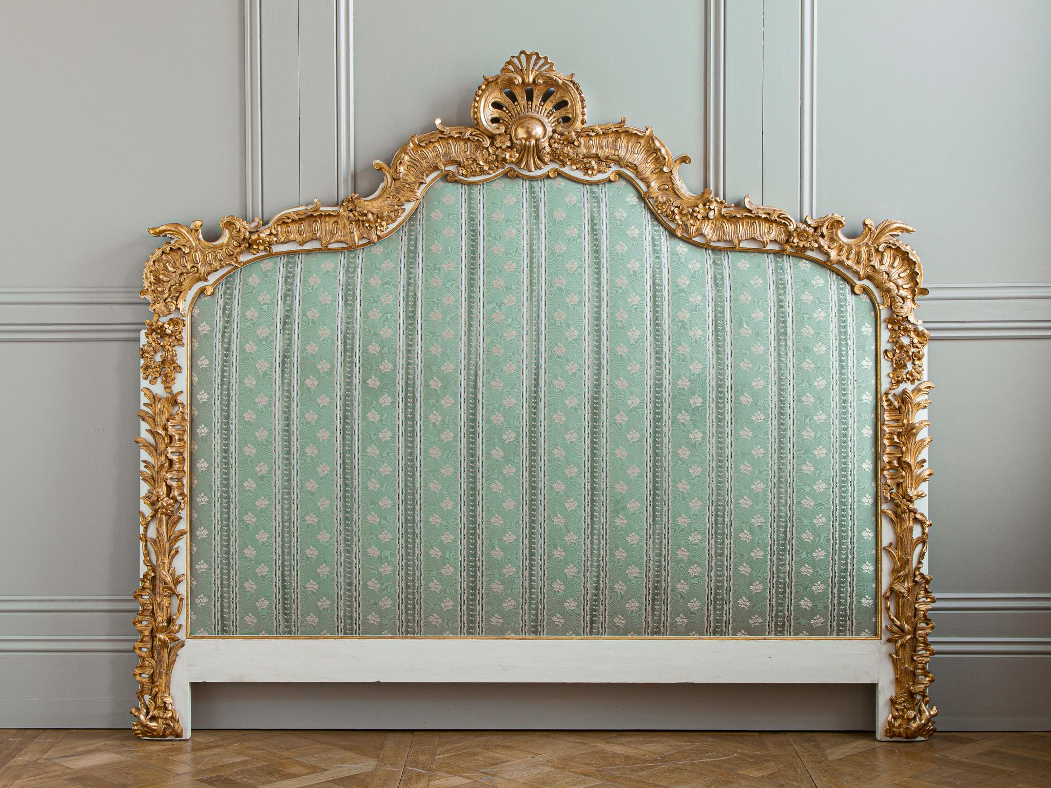 A large headboard from France, circa first half of 20th century with wonderfully ebullient carving in the Louis XV style featuring stylised acanthus leaves and small, detail-carved flowers, with an Art Deco styled rocaille shell at the apex. 
The
