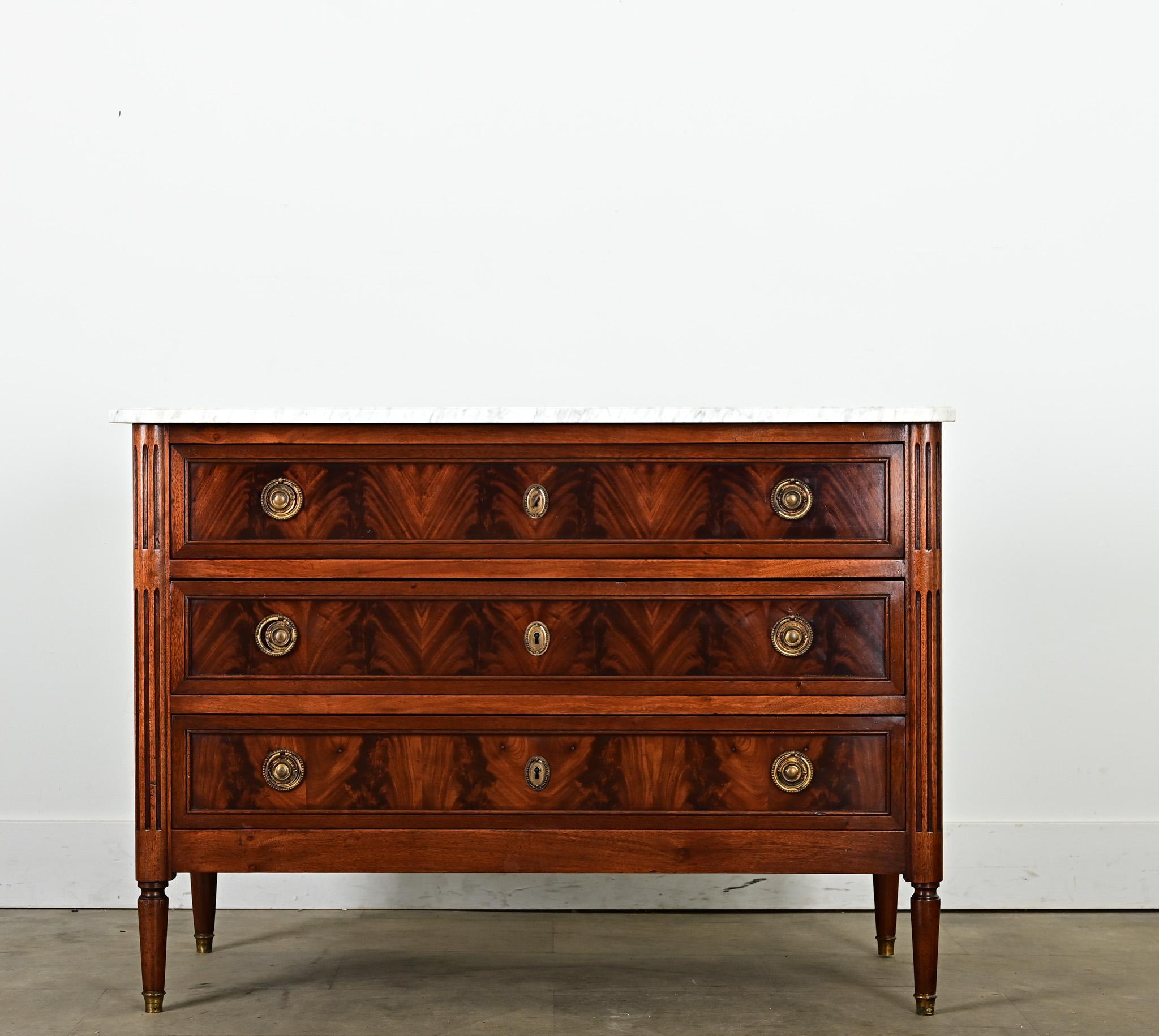 An elegant Louis XVI-style commode from France, early 20th century, its mahogany case has been recently refinished to fully appreciate the stunning, flamed effect over the wide drawers. The white marble top is traced in a fine web of gray veining,