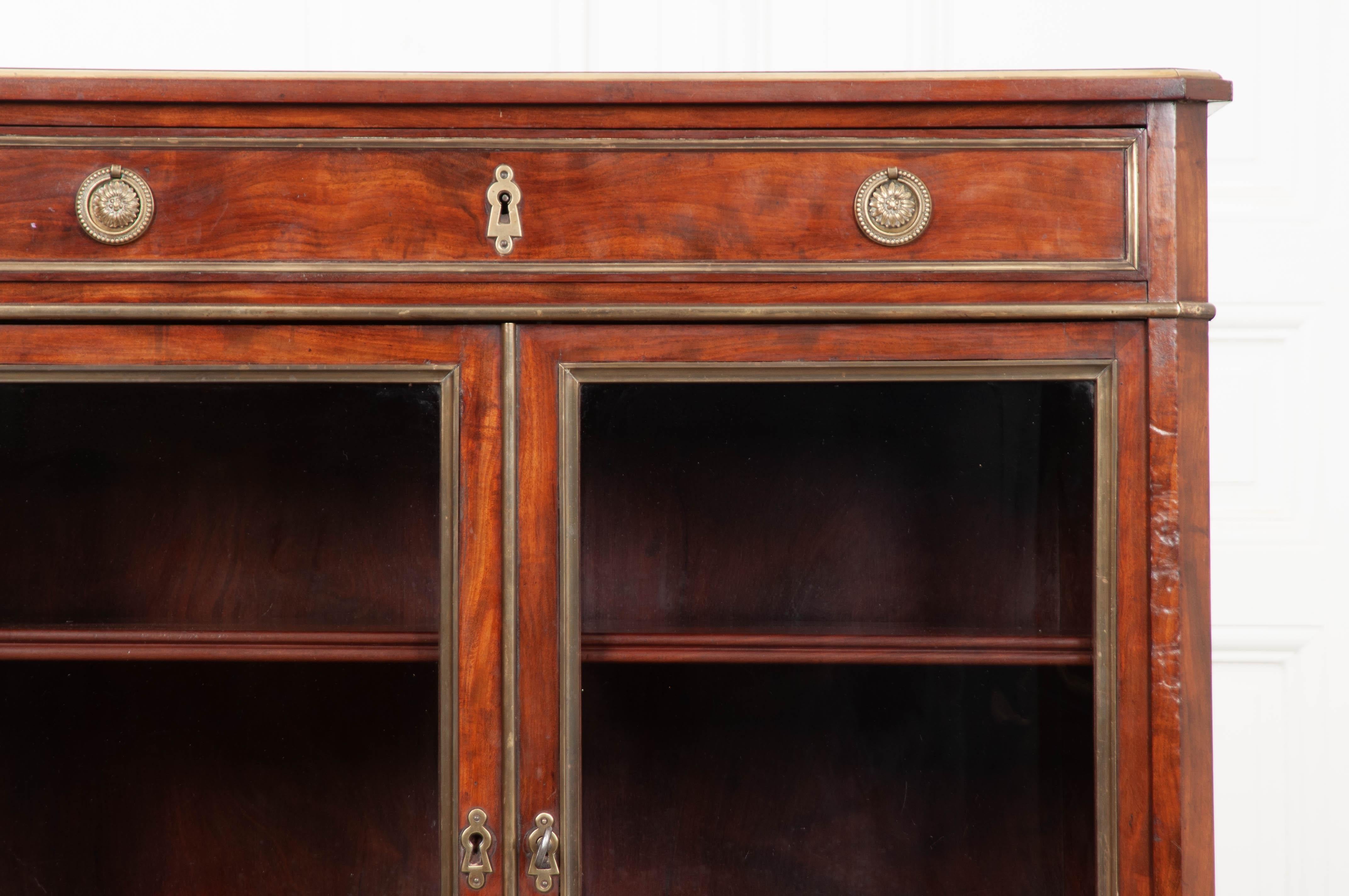 Beautifully toned mahogany was carefully selected when creating this beautiful vitrine from the early part of the 20th century. The antique case piece is comprised of a single wide drawer that sits over two glass-front doors. Both the drawer and