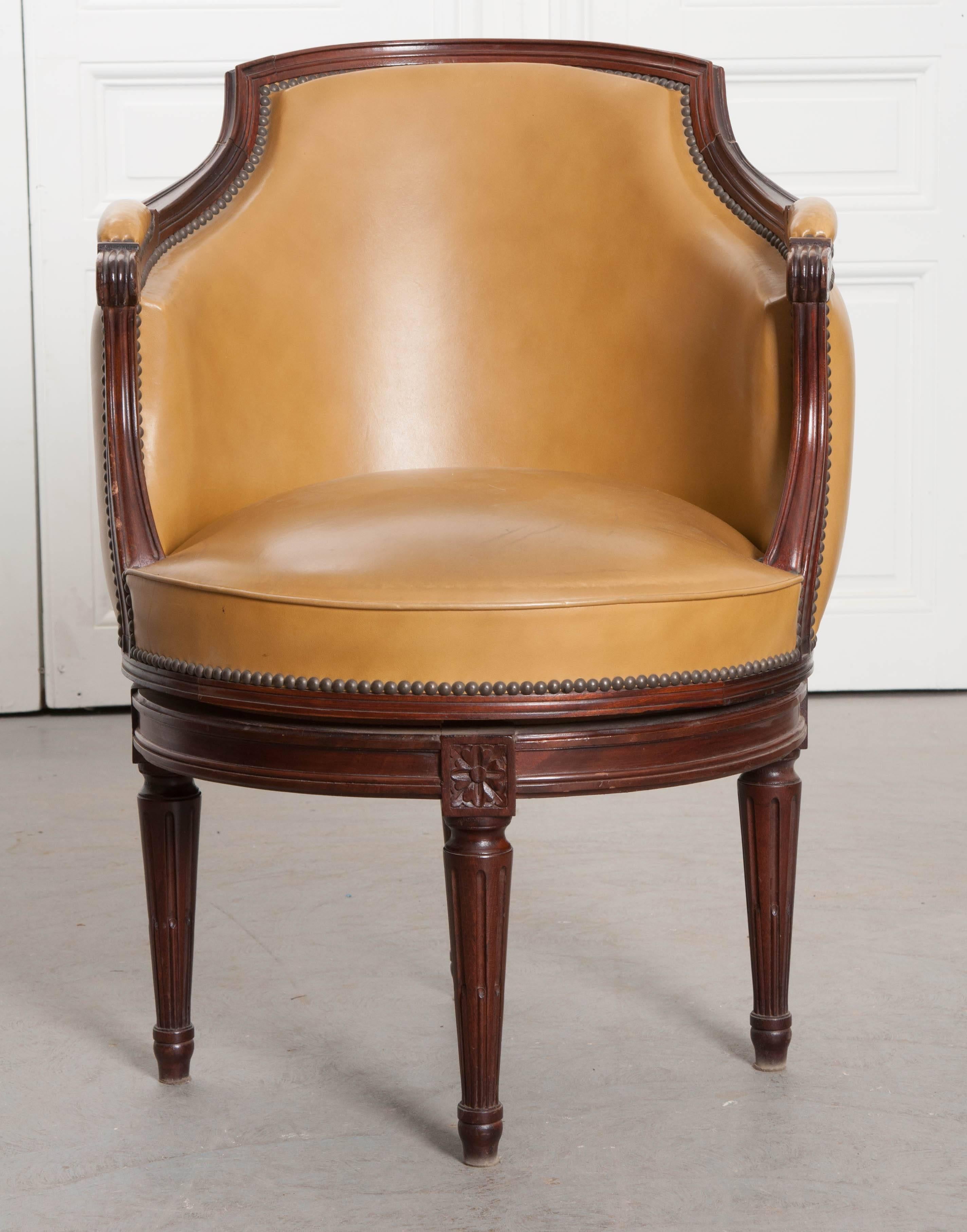 An individual mahogany swivel chair, done in the Louis XVI style in France, circa 1910. The chair has a round base, to which the chair is mounted, allowing it to rotate in a 360-degree circular motion. The chair has a barrel back and is upholstered