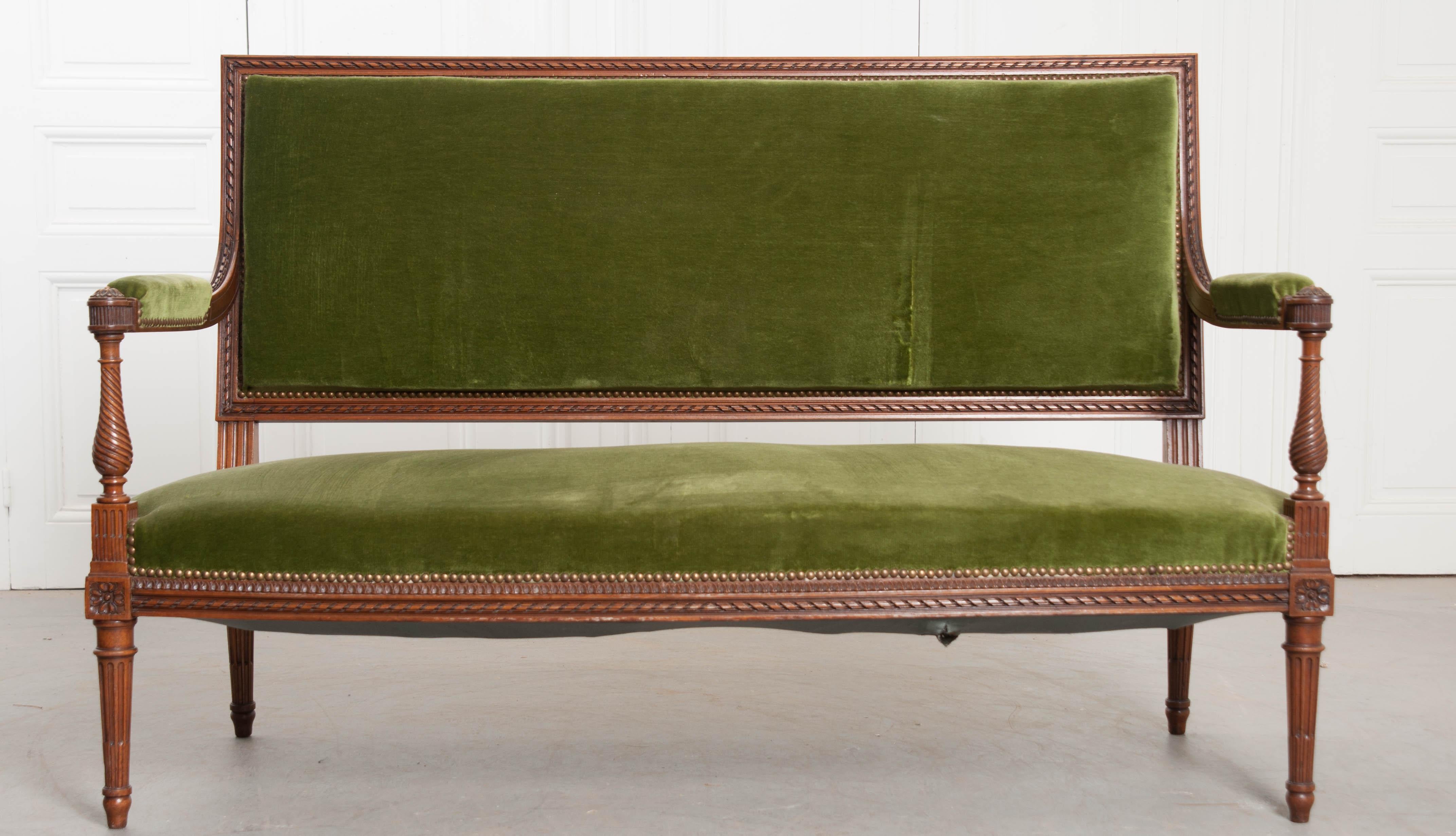 A fabulous green velvet upholstered Louis XVI style walnut settee, made in France, circa 1900. Magnificent carved details embellish nearly every square inch of the walnut frame. A carved, twisted ribbon motif runs the perimeter of the sofa’s back,