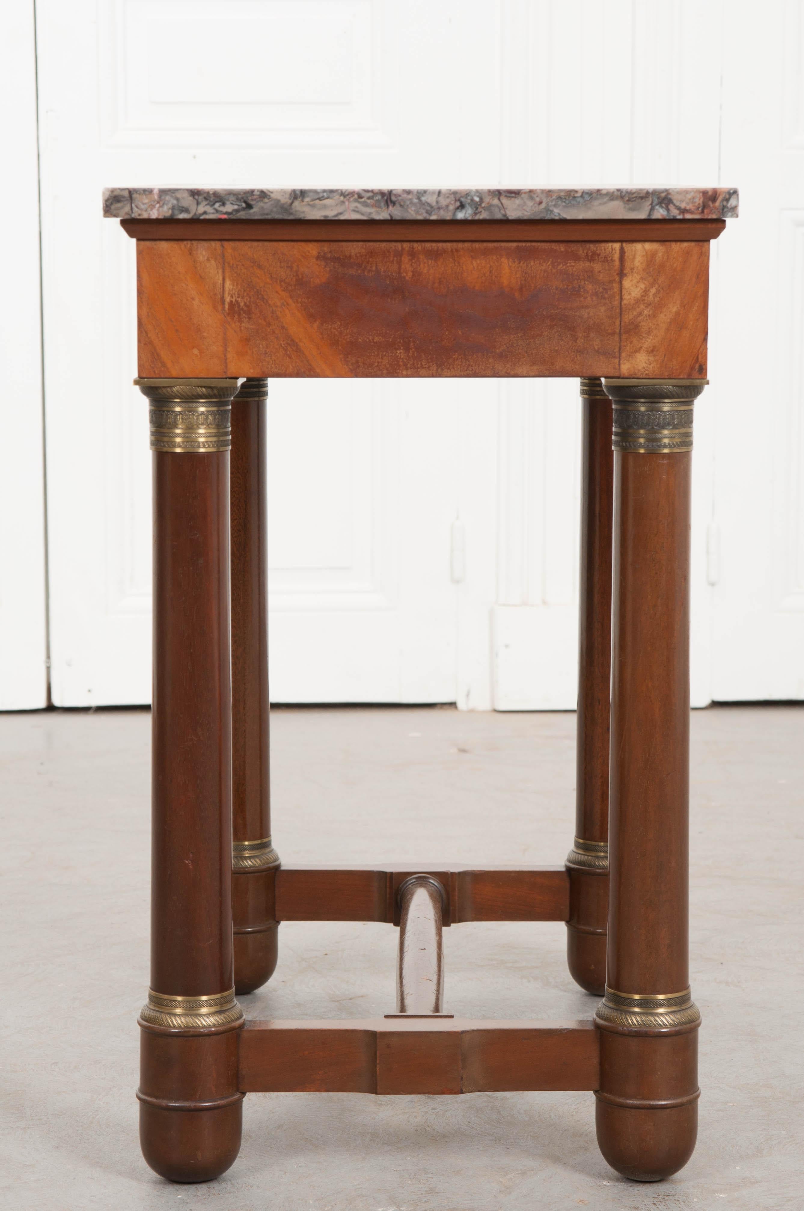 An Empirically styled mahogany side or occasional table, with exceptional marble top, from 1930s France. The multicolored marble top is in excellent condition with brilliant veins and coloration. Four column-form legs lift and support the top. They
