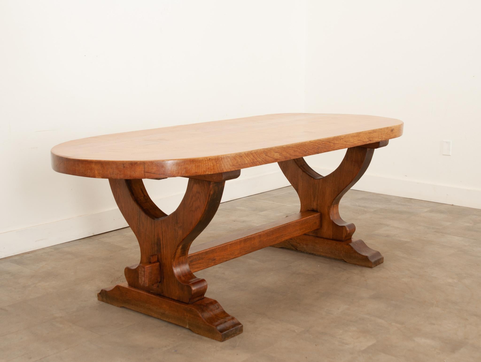 A French dining table from the early 1900s with a thick oak top and trestle base. At over 2-½” thick, the impressive top has a capsule shape and rests atop a substantial oak trestle base. This unique table would be wonderful in a breakfast or dining