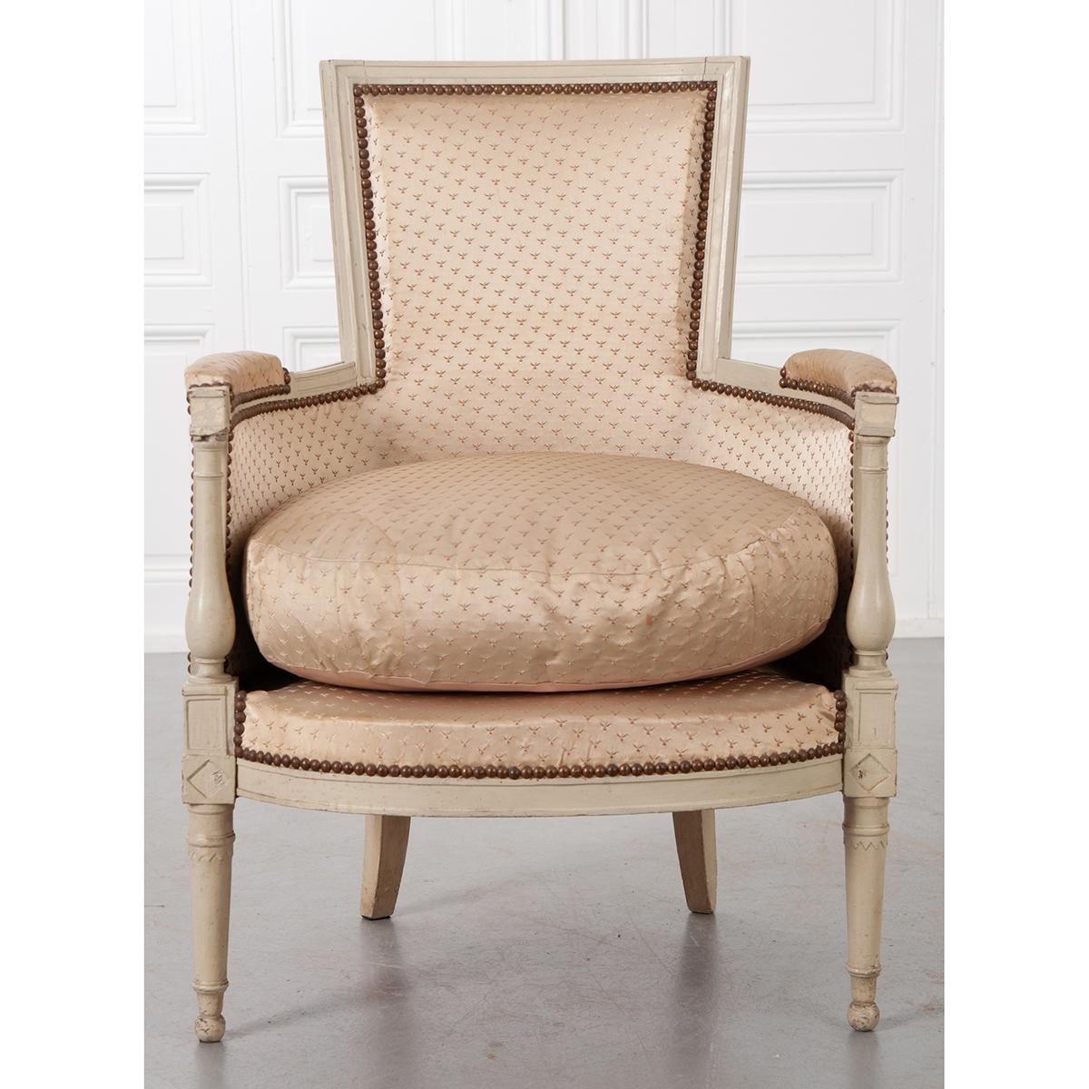 A fabulous early 20th century bergère, with taupe painted frame, made in the Directoire style in France, circa 1900. This beautiful, large chair has a linear back that is juxtaposed to its round seat. The chair is upholstered in a vintage silk