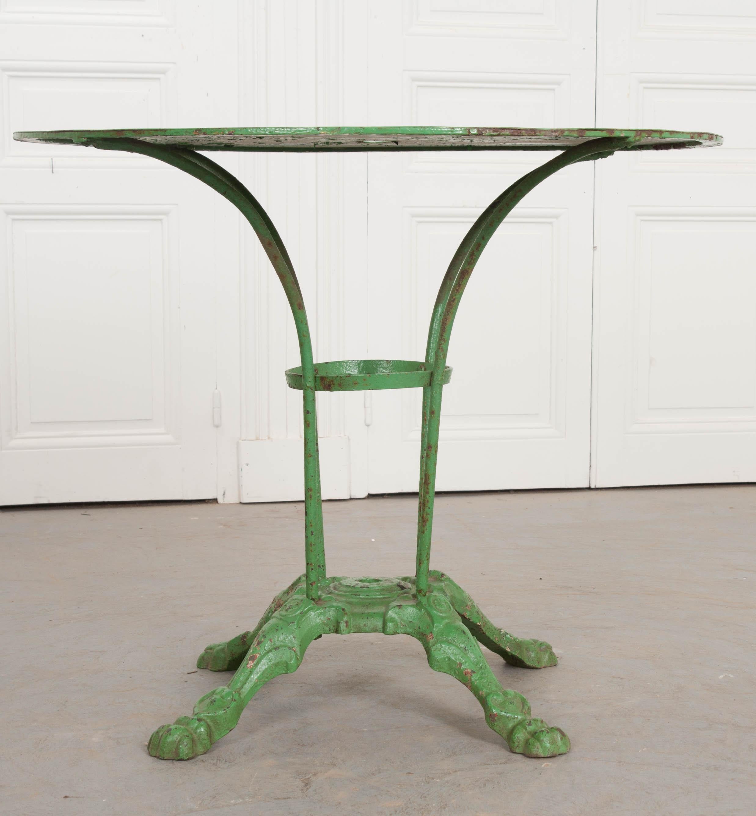 A 1900s iron and metal garden table, painted green, from France. The table has a classically styled cast iron base, with four paw feet and space for an umbrella. The metal top is in wonderful antique condition, with the antique green paint becoming