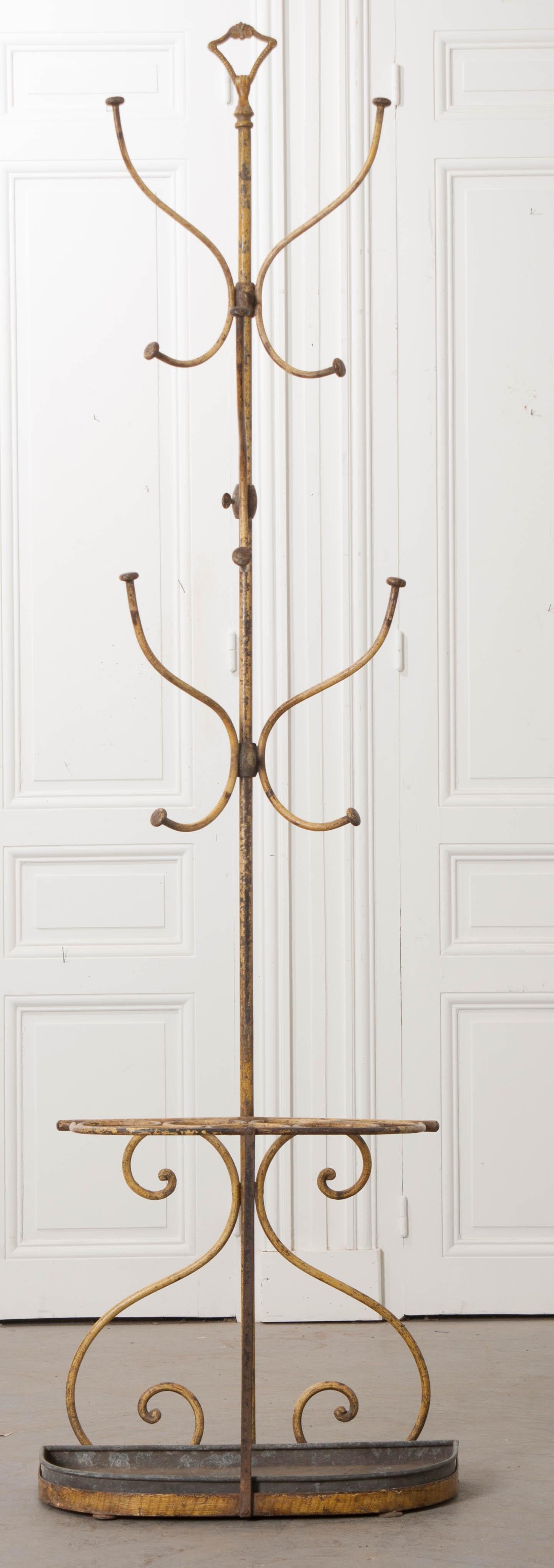 An outstanding metal hall tree, painted yellow, from 1900s France. The antique is made of cast iron, in restrained scrolled form. Five adjustable hooks provide places for hats, coats, and scarves, while space for up to seven umbrellas or parasols.
