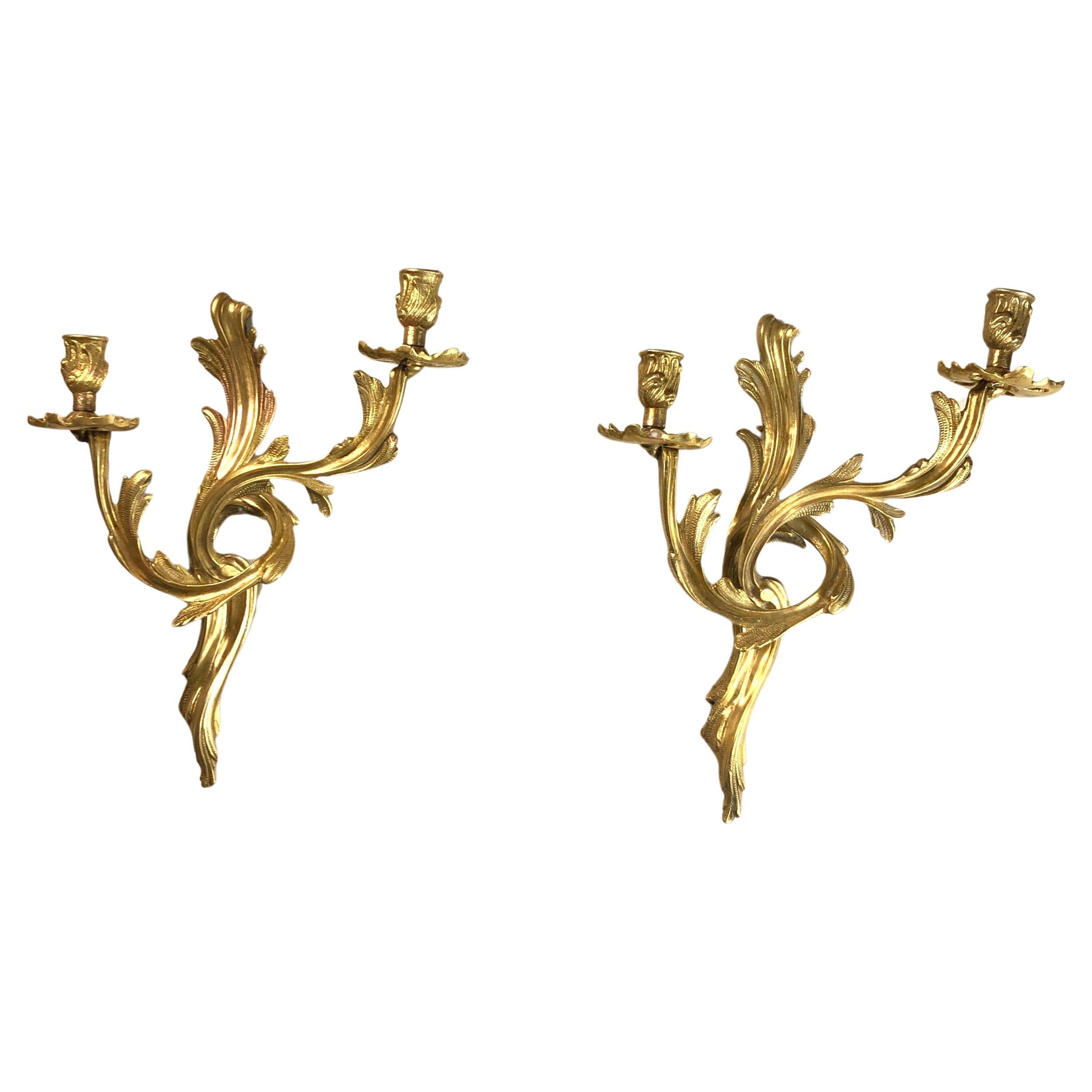 A French pair of cast brass double arm opposing antique wall sconces, the acanthus leaf scrolling arms with leaf bobeche drip pans and bulbous leaf candle sconces, issuing from a opposing acanthus leaf backplate, good original condition that has had