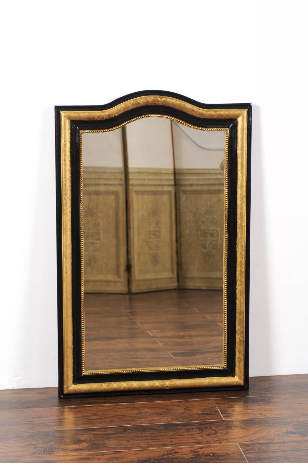 A French ebonized and gilt wooden mirror from the early 20th century with arched top and X-form motifs. This exquisite French mirror features an elegant rectangular silhouette, accented by a delicately arched top. The frame alternates layers of