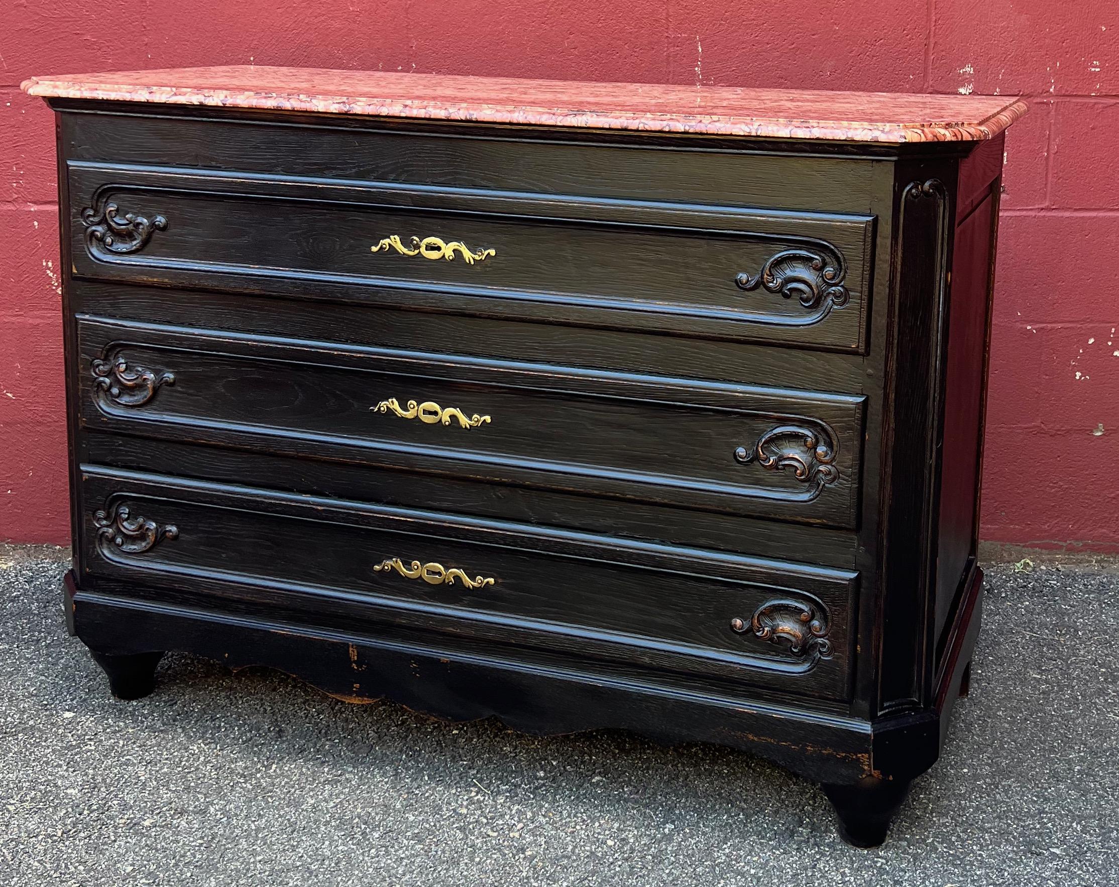 An elegant French 20th century chest of drawers with original brass details and a beautifully veined reddish marble top. The chest of drawers has been painted black but the patina gives this piece an updated “distressed” look. With dimensions of 36