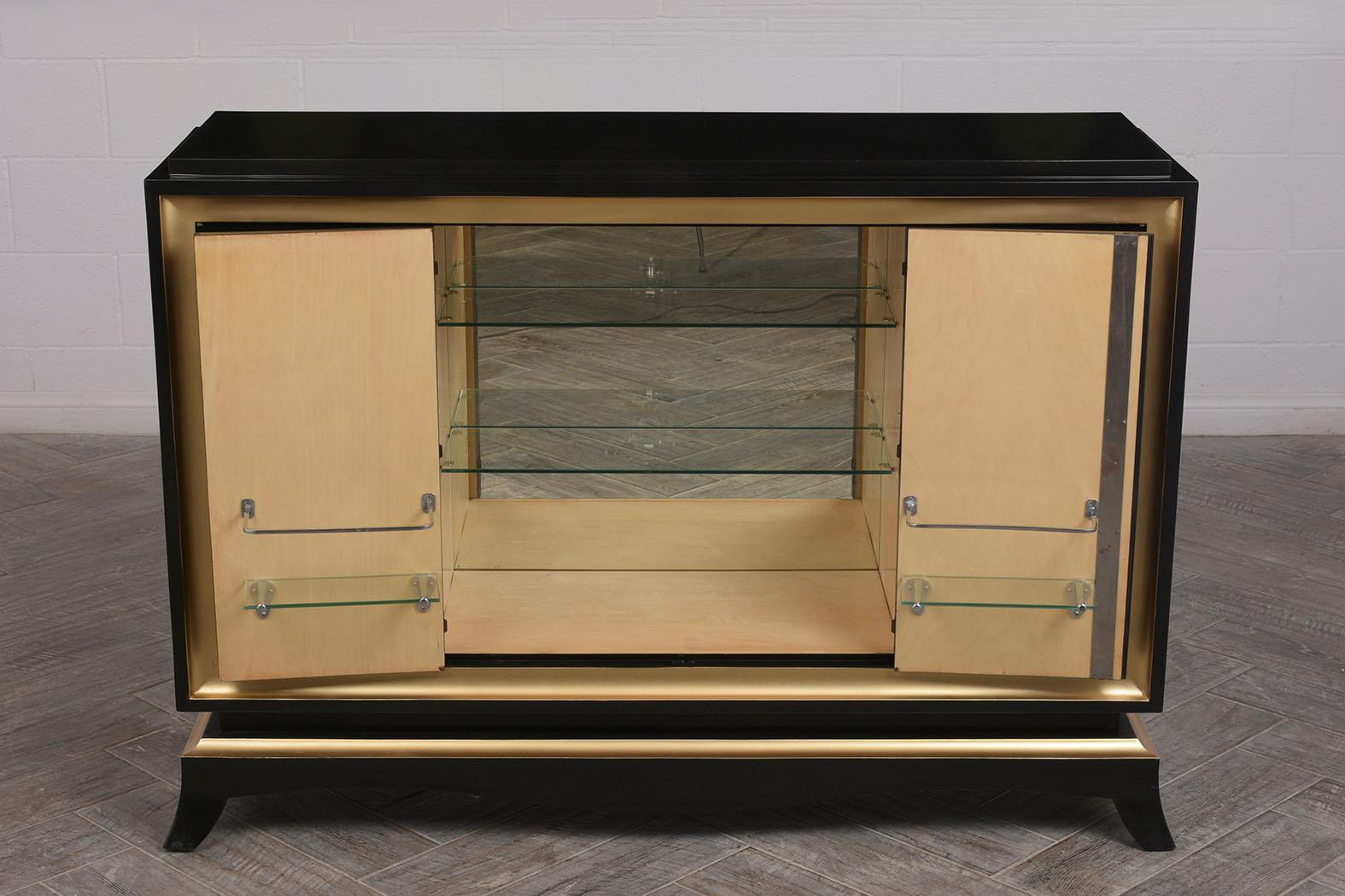 This beautiful 1930s French dry bar is made from solid wood with ebonized and gold gilt accent finish. There are two cabinet doors that fold to open with three sections inside. The two outer sections have two adjustable wood shelves and the