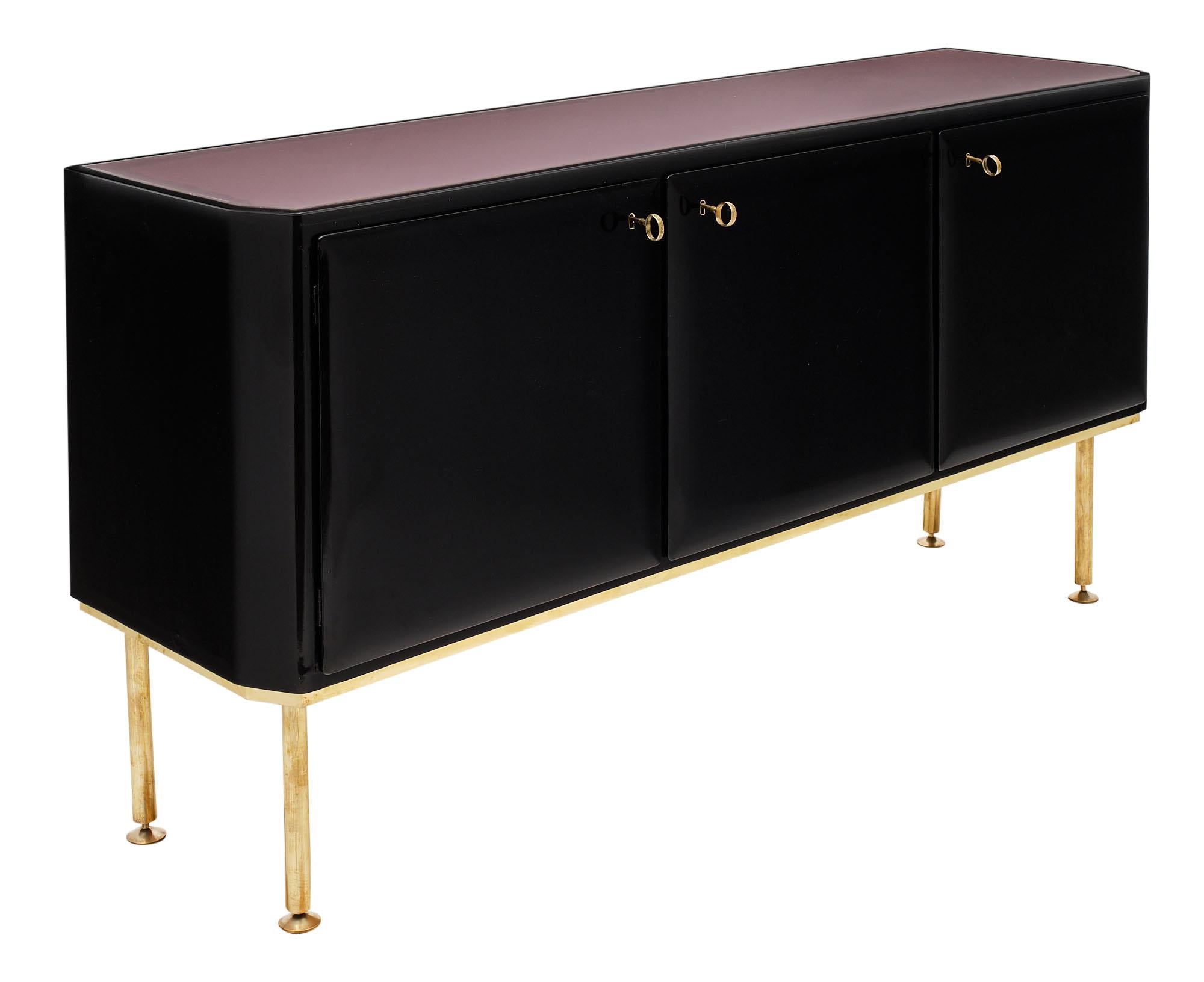 French buffet or enfilade made of ebonized cherry wood and featuring a lustrous French polish finish. There are three doors which open to shelving inside. It is supported by adjustable gilt brass legs and the top has a beautiful pink-purple glass