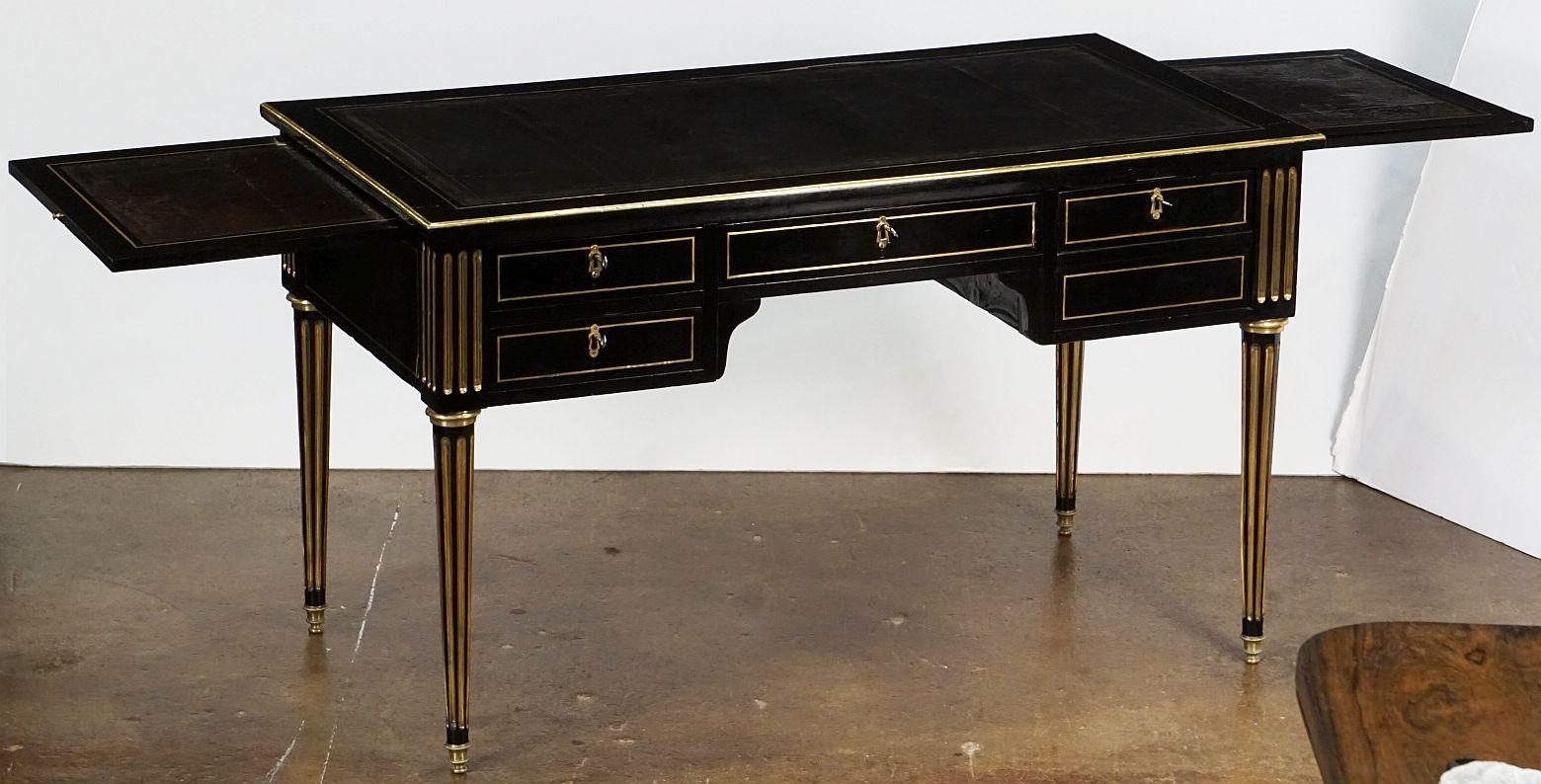 An elegant French bureau writing desk (or table) of ebonized mahogany, in the Louis XVI style, featuring an embossed leather top with gilt bronze accents over a frieze with fitted drawers, with two 17