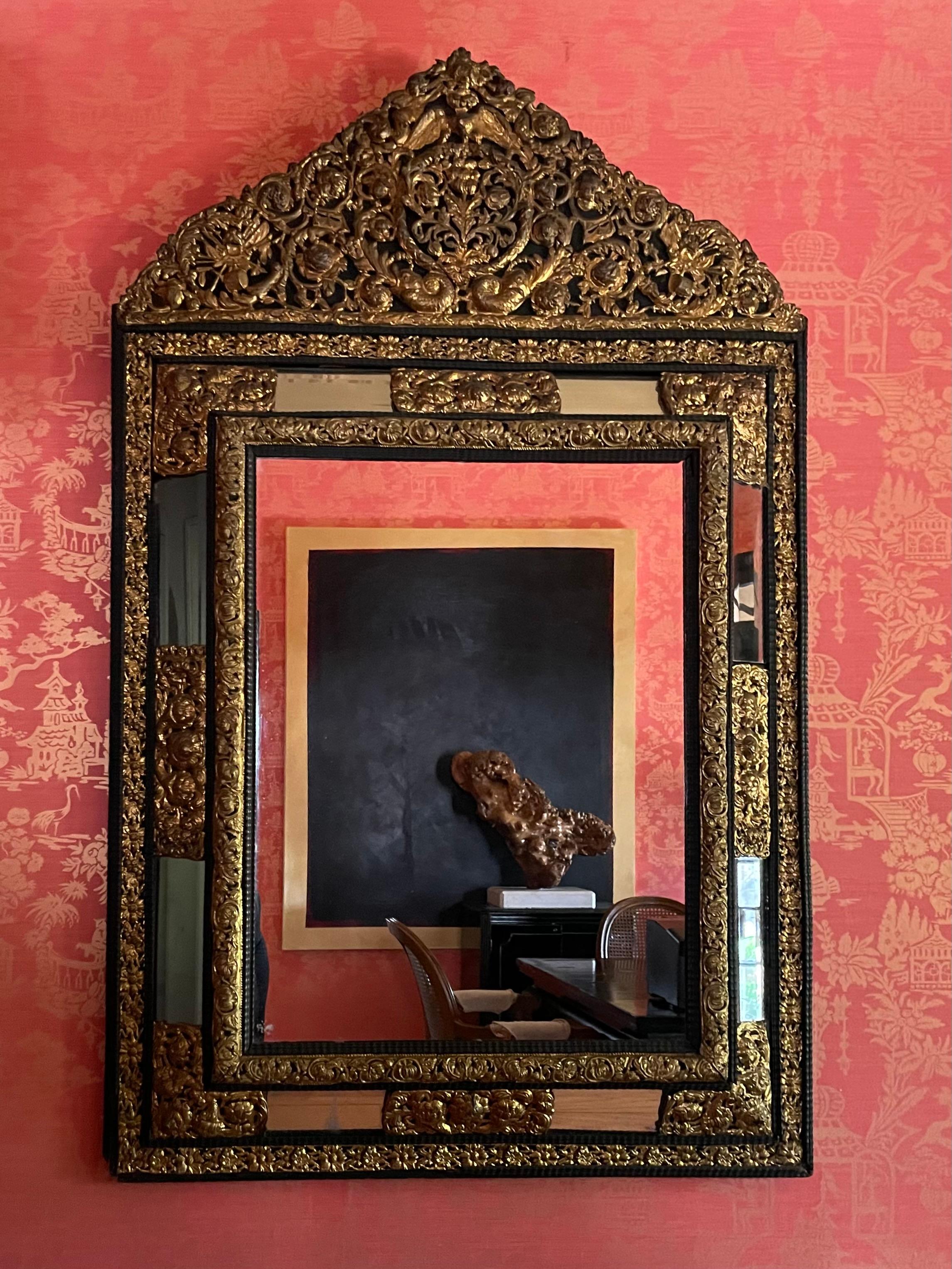 A monumental, stunning, and beautifully designed French Ebony repousse brass mirror with beveled glass. Hand-hammered with intricate French angels, drums. A very substantial and important look. The mirror is 75 pounds in weight. (A very small and