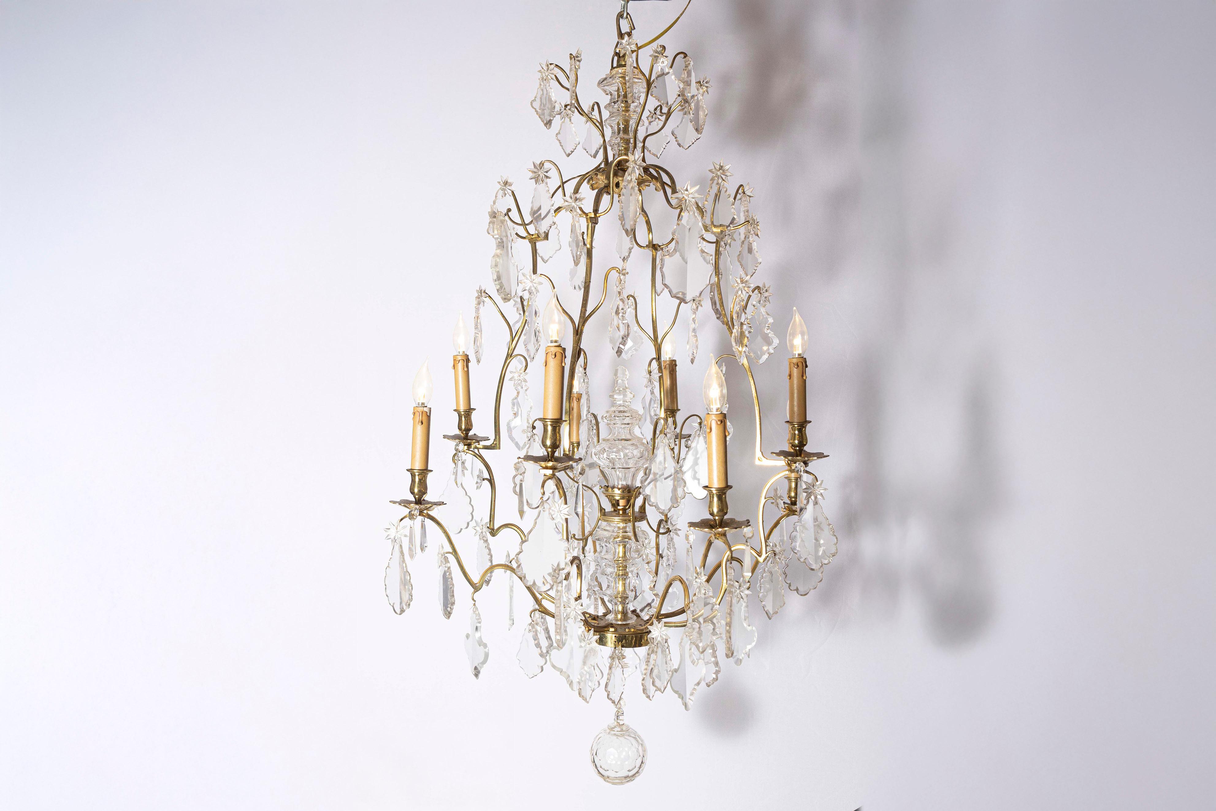 Lampadario francese a otto luci in cristallo dell'inizio del XX secolo, con armatura in metallo dorato e pendagli. Nato in Francia durante la fine del secolo, questo squisito lampadario è caratterizzato da un'armatura in metallo dorato che sostiene