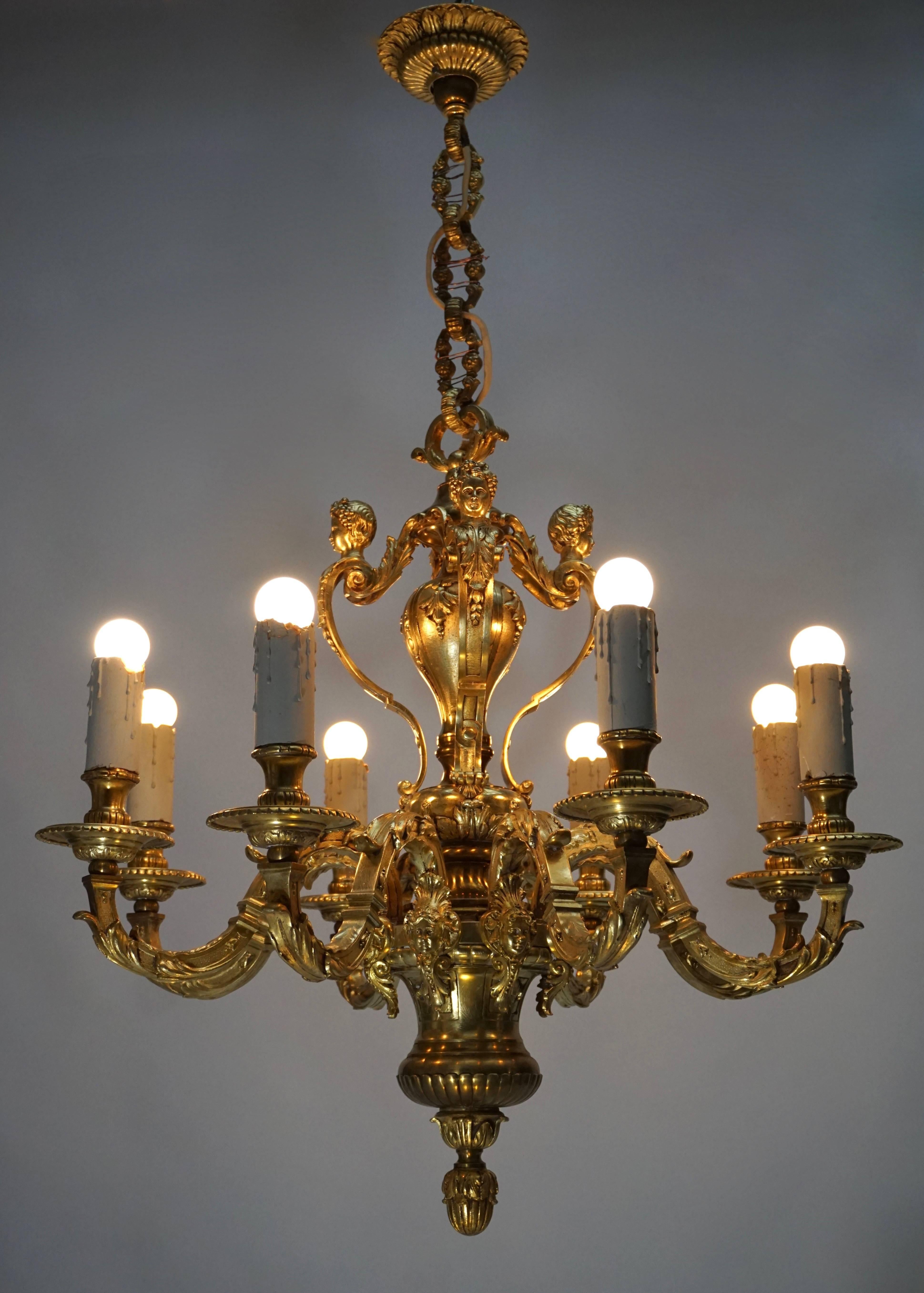 This massive Louis XV style bronze chandelier was created in Avignon, France, circa 1950. The light fixture features four cherubs on the upper part with crossed torches, fleurs de lys and other cartouches and eight angel faces below with scroll