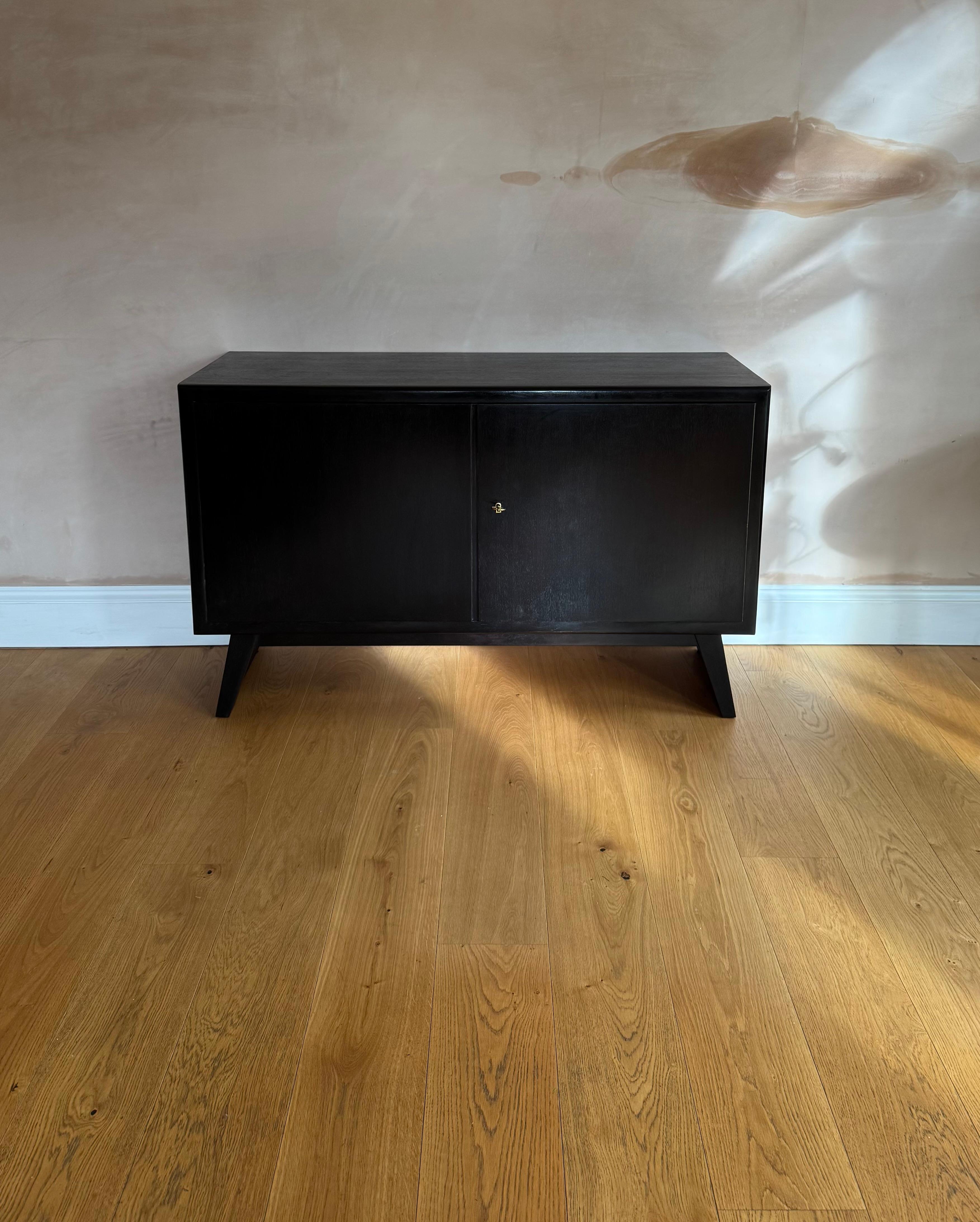 An elegant two door ebonised small cabinet on splay legs with original key and lock. The cabinet has been rebonised. In good condition with minor surface scratches. 