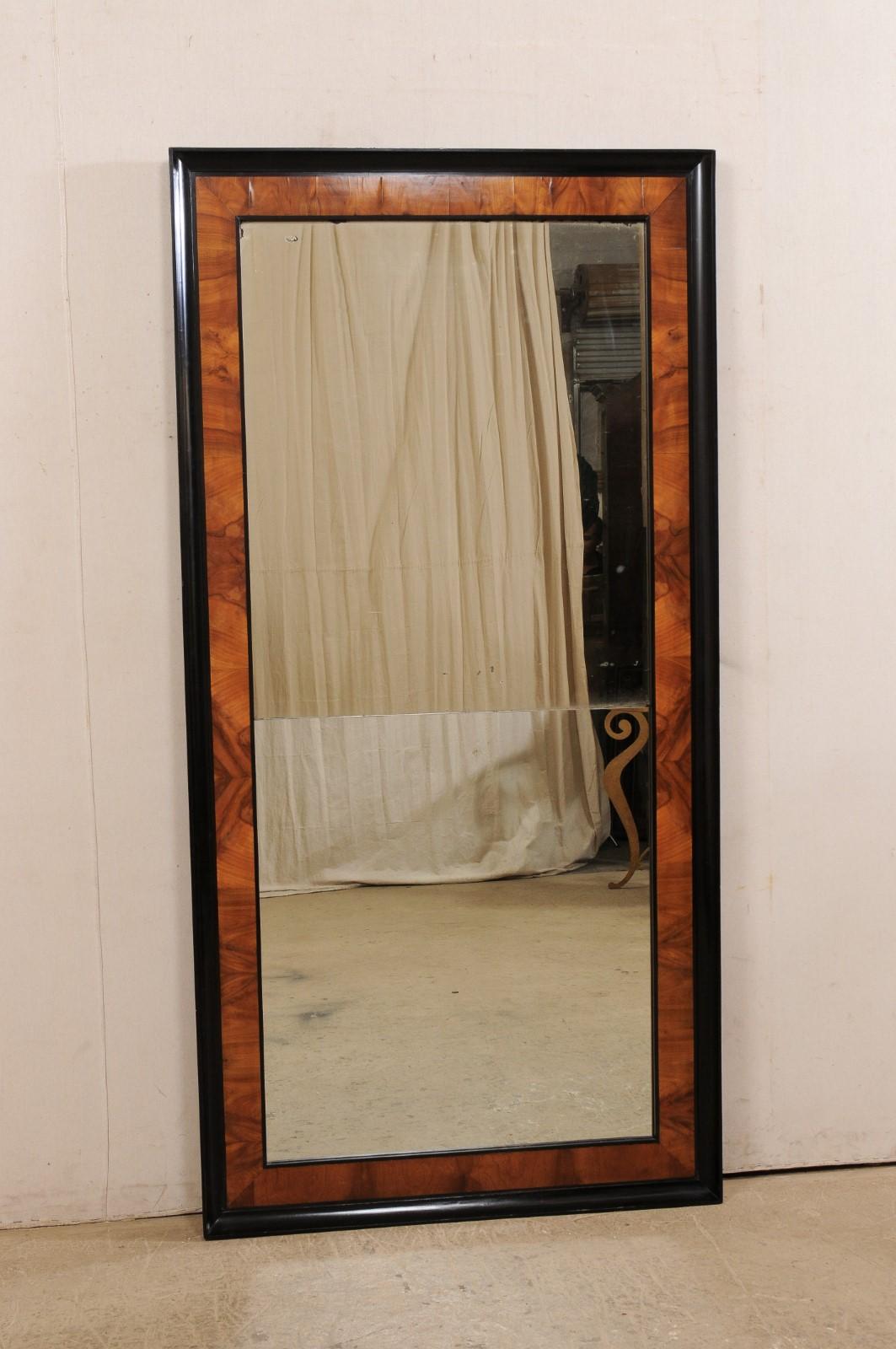 A tall French wall mirror from the early 19th century. This antique mirror from France is rectangular-shaped and designed with clean, minimalist lines. It features an elegant two-tone surround with black molding about the outer frame and a think