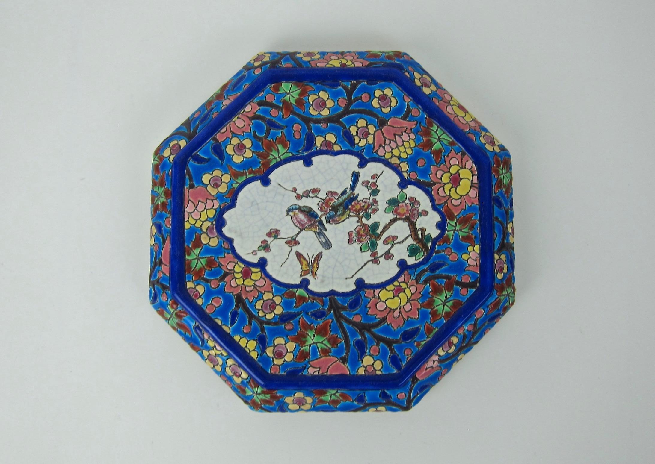 A colorful French faience trivet or stand from the Emaux de Longwy art pottery workshop in France. The vintage ceramic stand rests on four feet and is an octagonal shape designed for display and use on a tabletop. 

The vivid enameled glaze in a