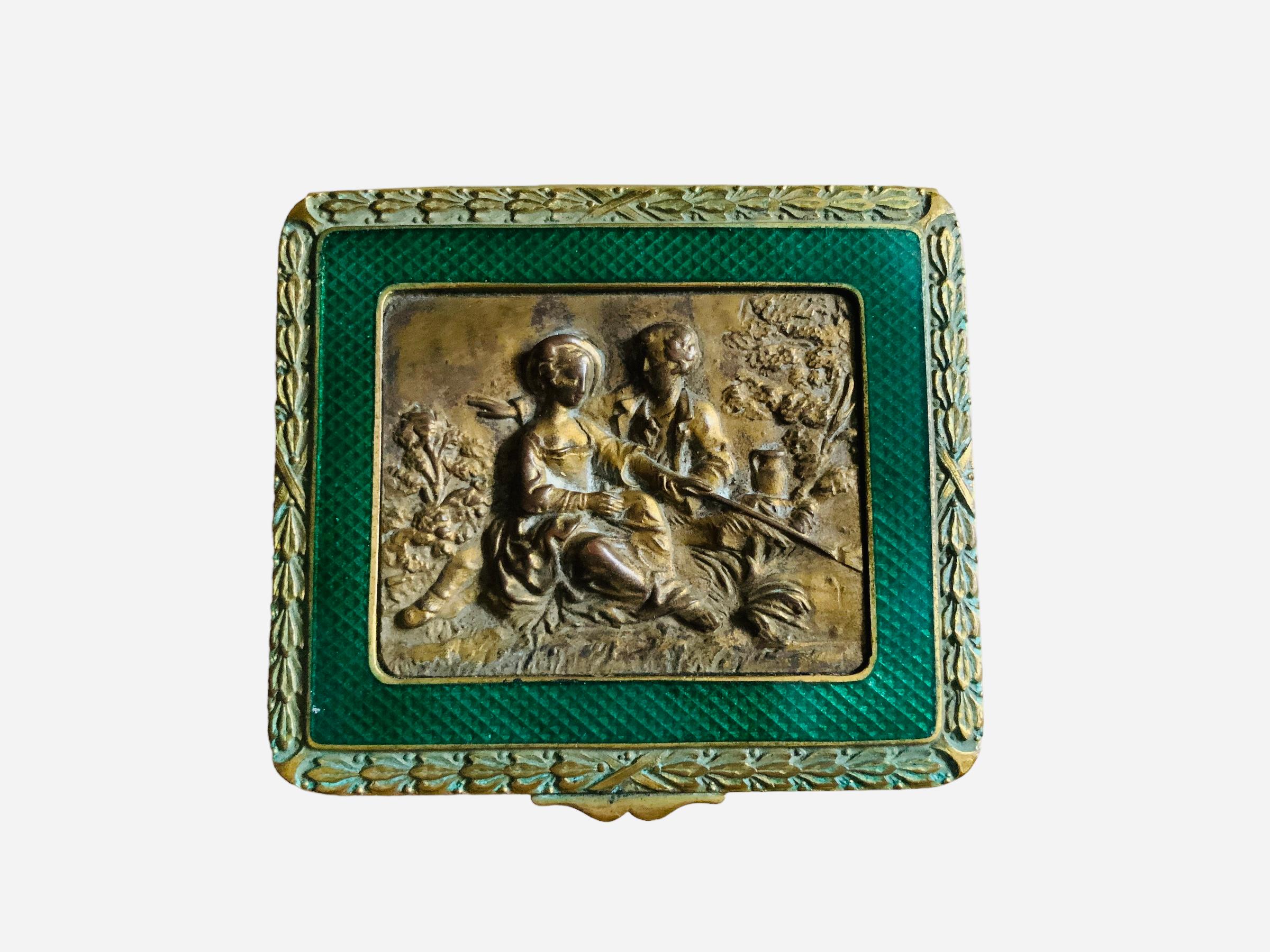 This is a French bronze metal square hinged lidded box. It depicts a lid decorated with an 19th century country relief scene of a romantic couple. The gentleman is hugging a lady while they are seated in the grass beside a tree. The relief is