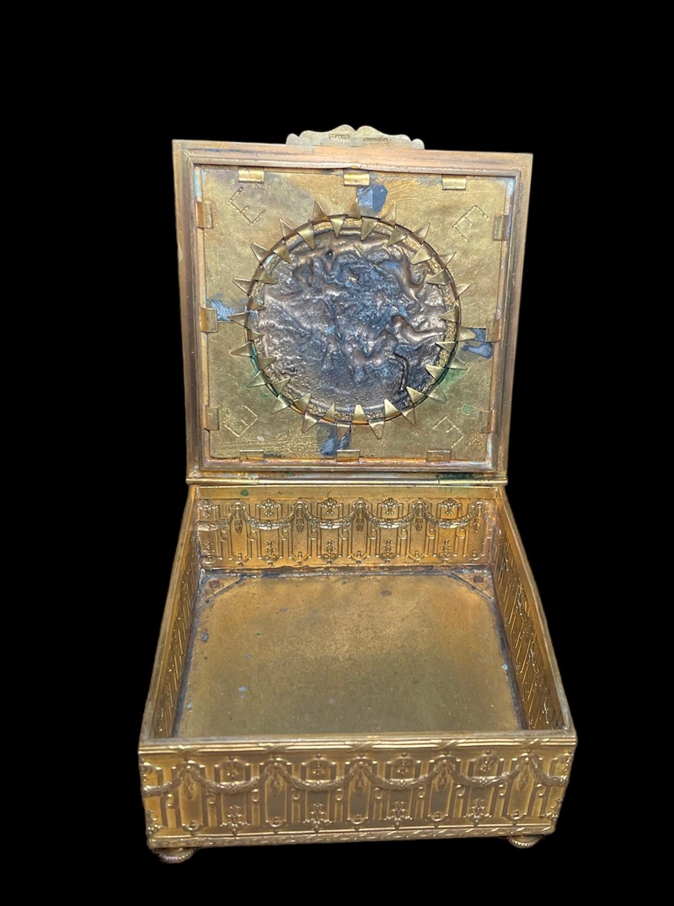 This is a French bronze metal square hinged lidded box. It depicts a lid decorated with an 18th century country relief scene of two ladies and a gentleman playing with a dog while another dog is barking to some birds. The relief is enhanced by the