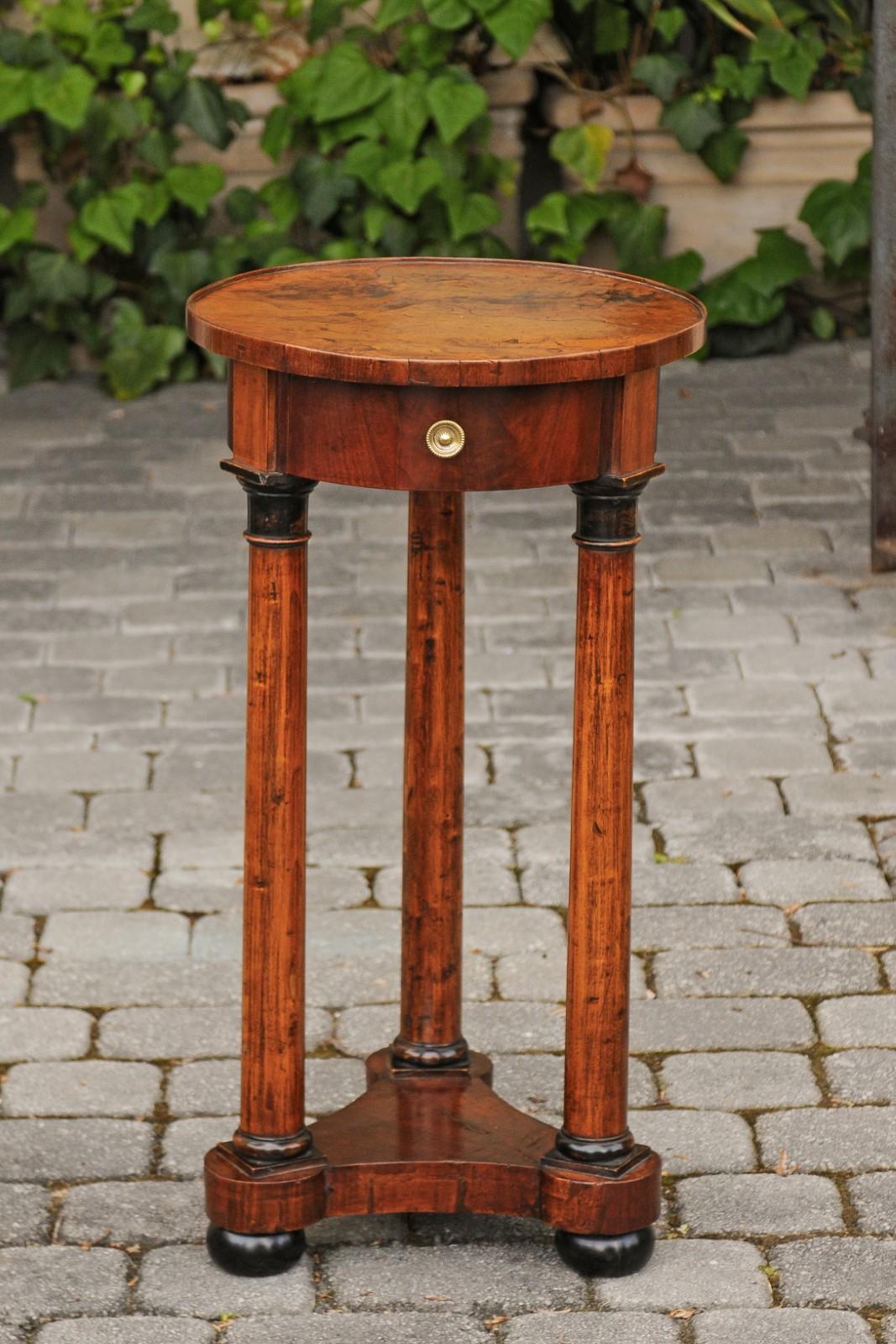 A French Empire walnut pedestal table from the early 19th century, with single drawer, Doric capitals, lower shelf and bun feet. Born in France during the early years of the 19th century, this exquisite guéridon features a circular top, adorned with