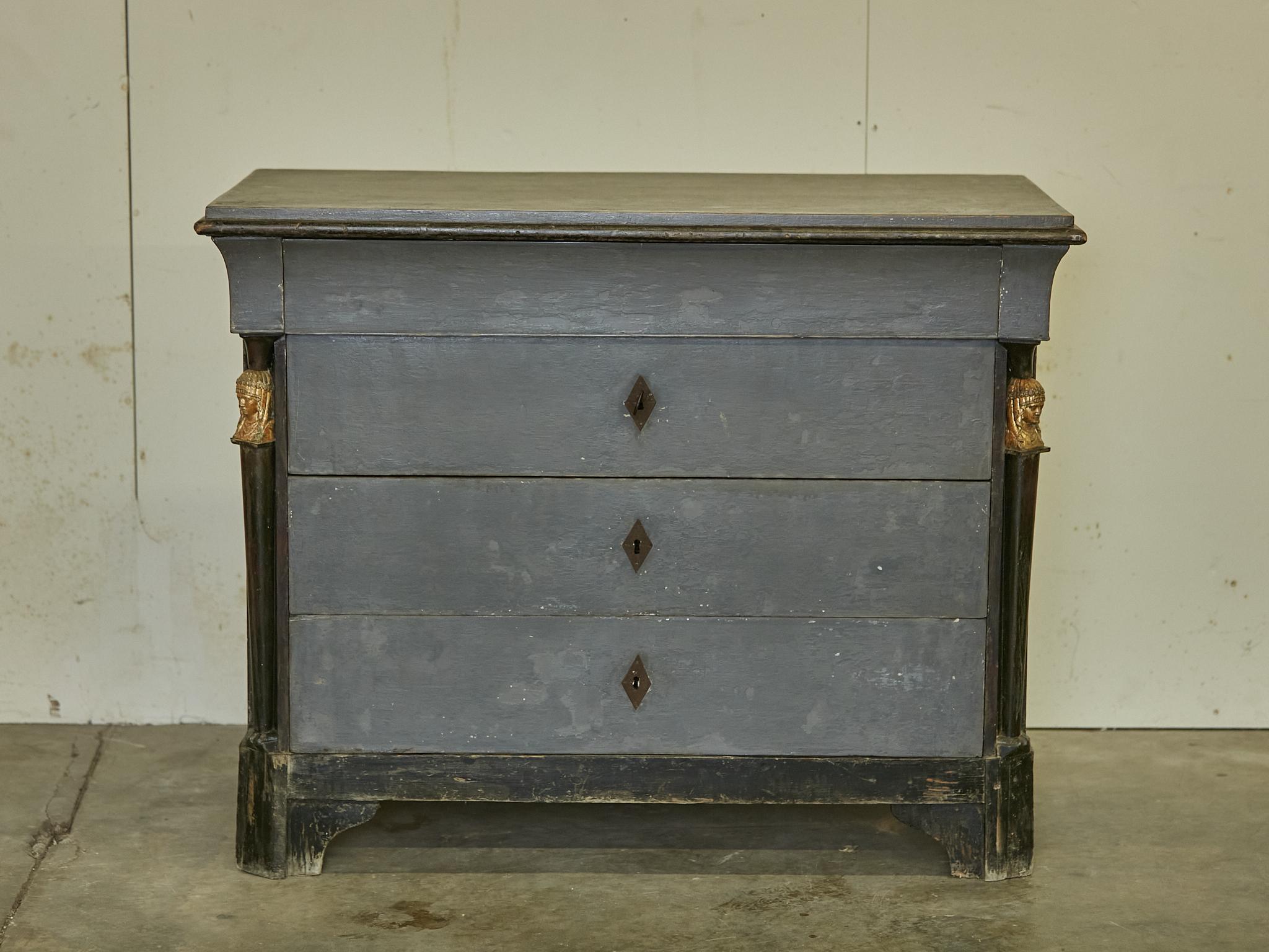 A French Empire style painted wood four-drawer commode from the 19th century with ebonized columns, carved giltwood female busts and bracket feet. Step into an era of refined elegance with this exquisite French Empire style painted wood four-drawer