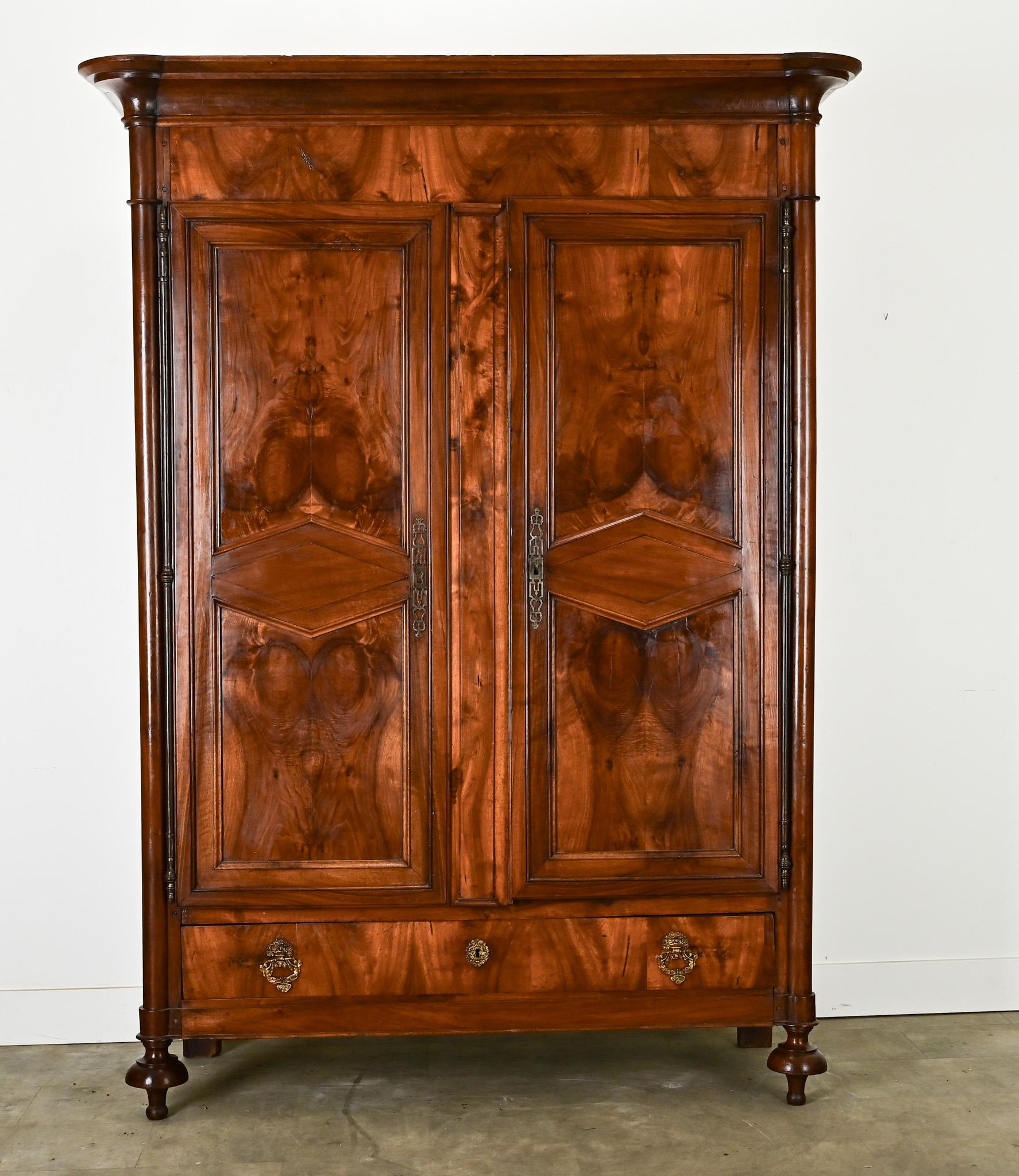 An impressive French Empire armoire built in the 1800’s. The pronounced cornice makes a statement above the pair of paneled and carved doors all made of solid bookmatched walnut with diamond shaped panels. The doors open on long steel barrel hinges