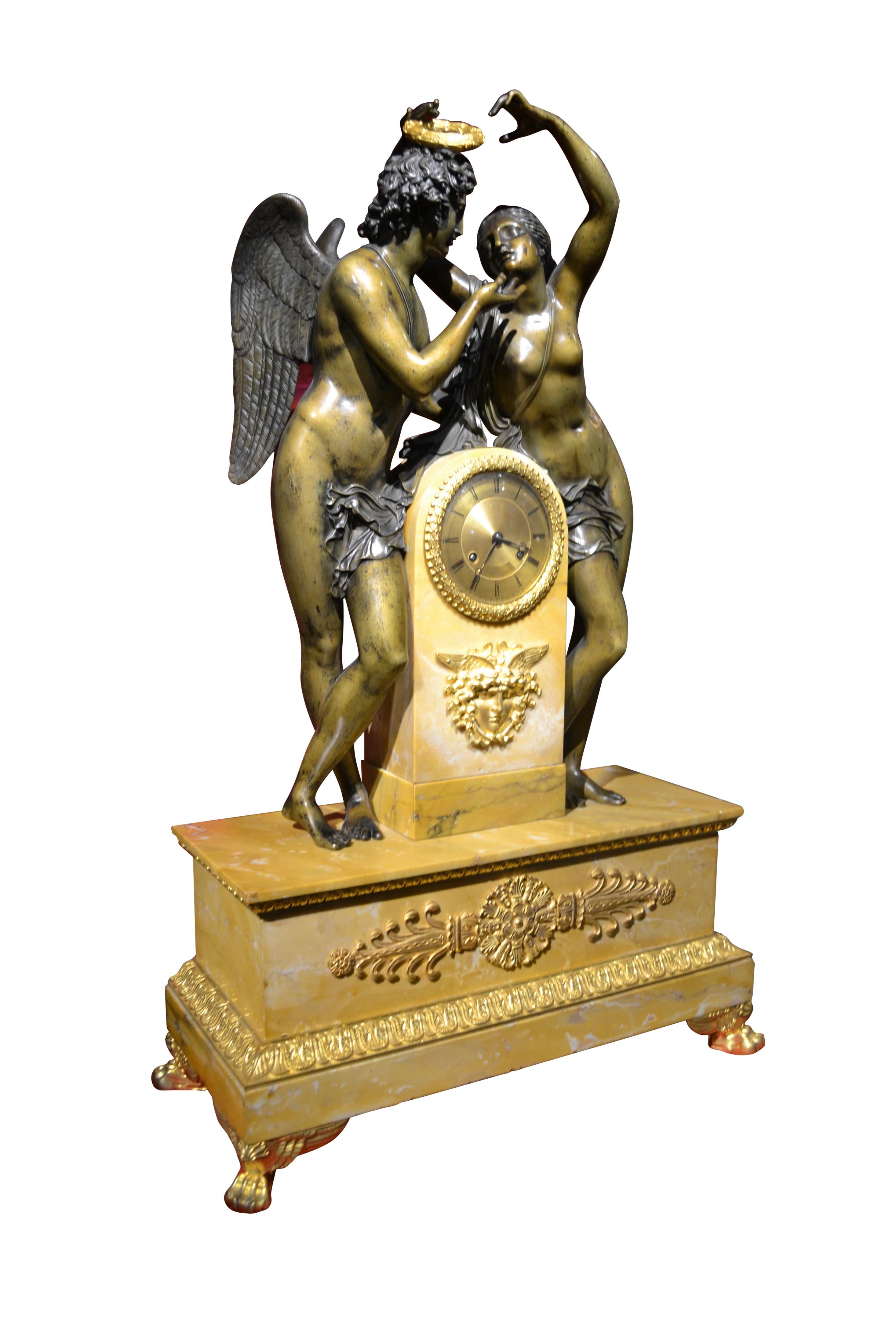 A large scale French Empire figurative allegorical clock showing “Psyche Crowning Amor”. Psyche stands to the right of the domed clock plinth, holding her hands aloft with a gilded wreath, (not shown), Amor stands to the left. The stepped yellow