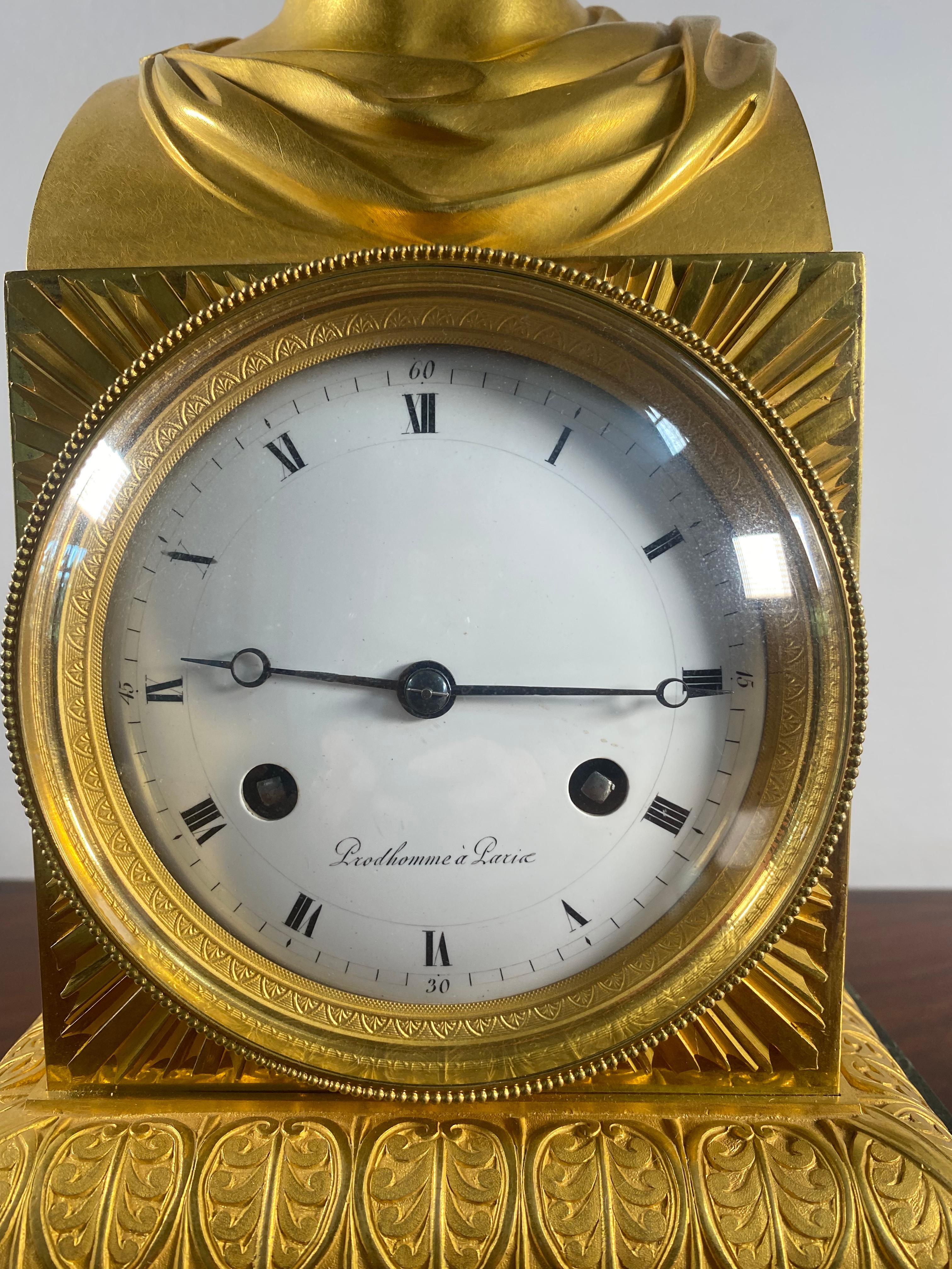 A period Empire Apollo Belvedere mantle clock in gilt bronze, the rectangular plinth on a stepped base richly decorated with acanthus. The plinth itself houses the large white enamel dial signed “Prudhomme a Paris”; the original movement with