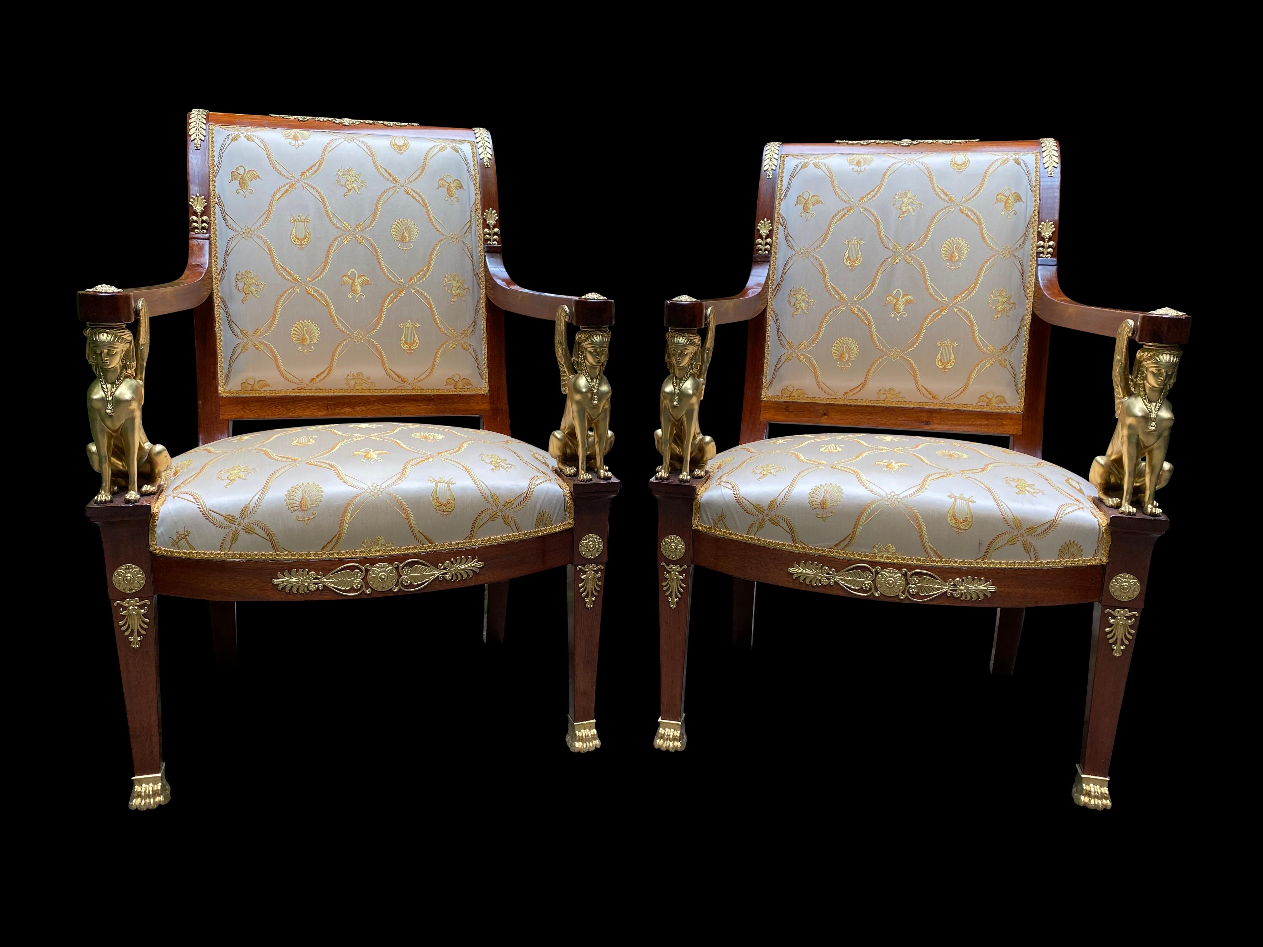 A stunning pair of French Empire armchairs with bronze mounts, 19th century. Napoleon III style mahogany armchairs with ormolu mounts, lion gilt paw feet, arms rest on seated sphinx gilt bronze supports. White and gold silk upholstery with classical