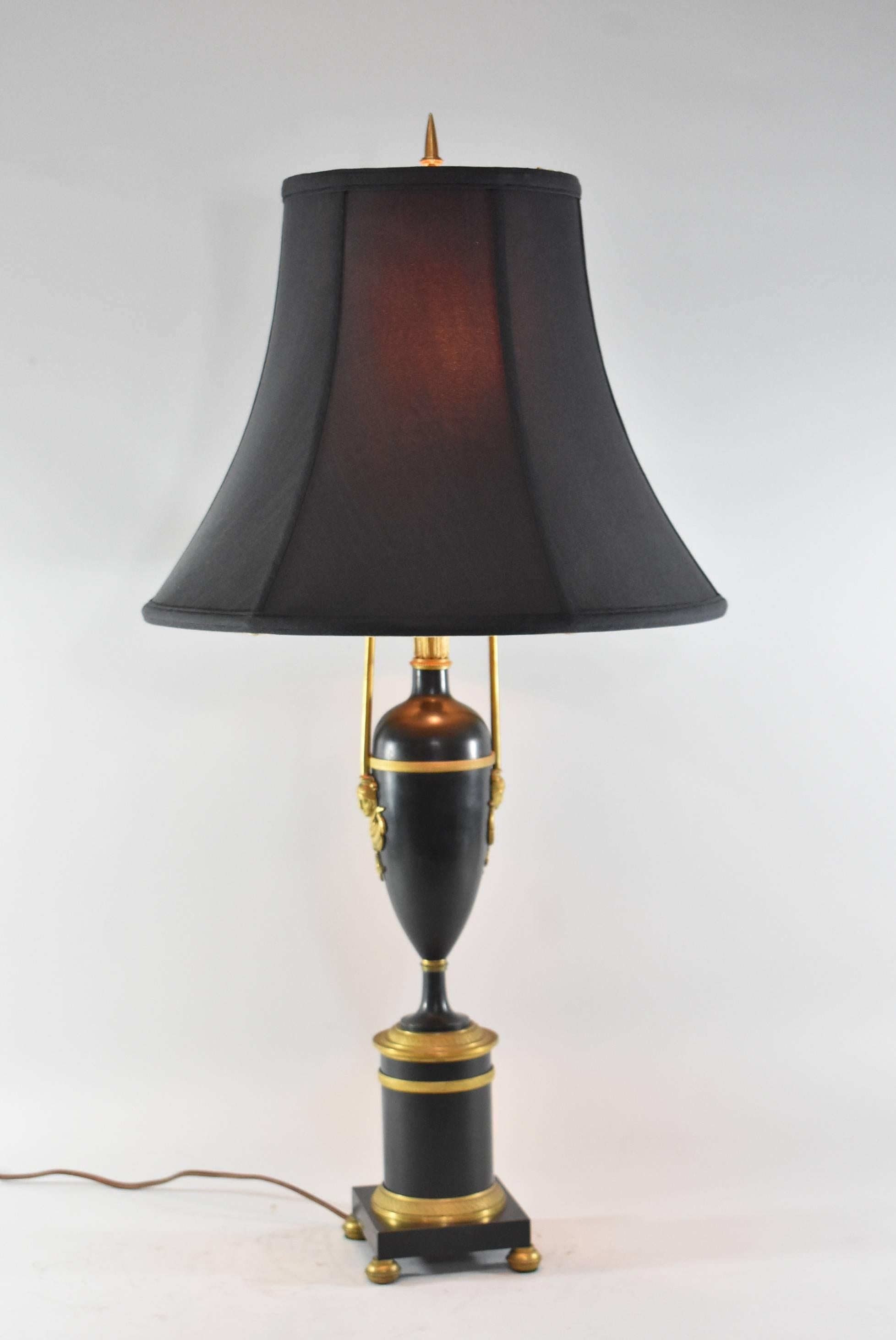 A great French Empire style lamp. Lamp has two sockets with pull chains. Black urn has bronze mounts on side in shape of Egyptian women. The urn sits on a cylindrical base with bronze accents which sits on a square base with four bronze bun feet.